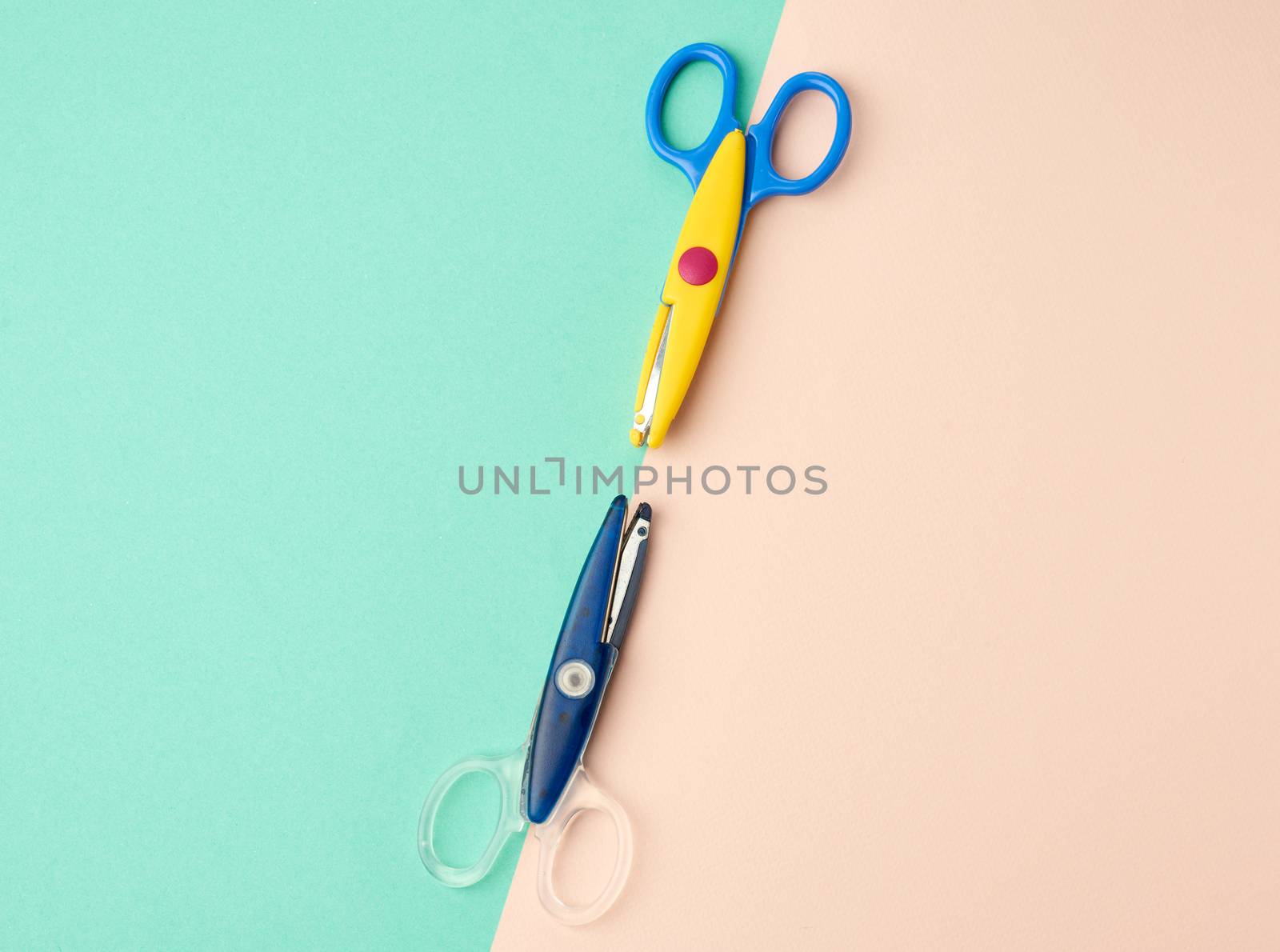 two pieces of plastic baby scissors for scrapbooking on a green background, copxy space