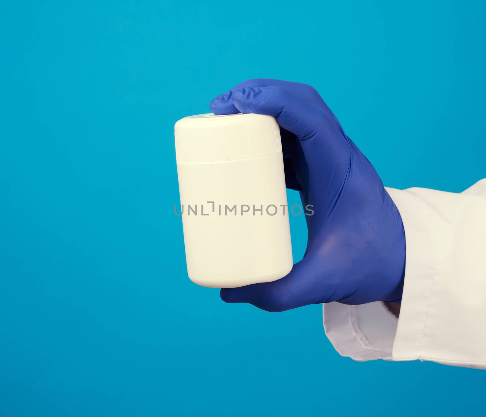 male doctor in a white medical coat and blue latex gloves holds a white plastic jar of pills, close up