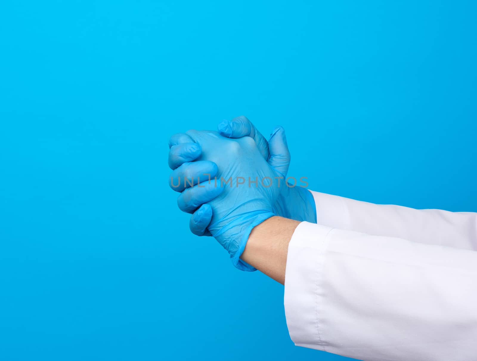 two hands in blue latex medical gloves joined in a handshake on a blue background, support concept
