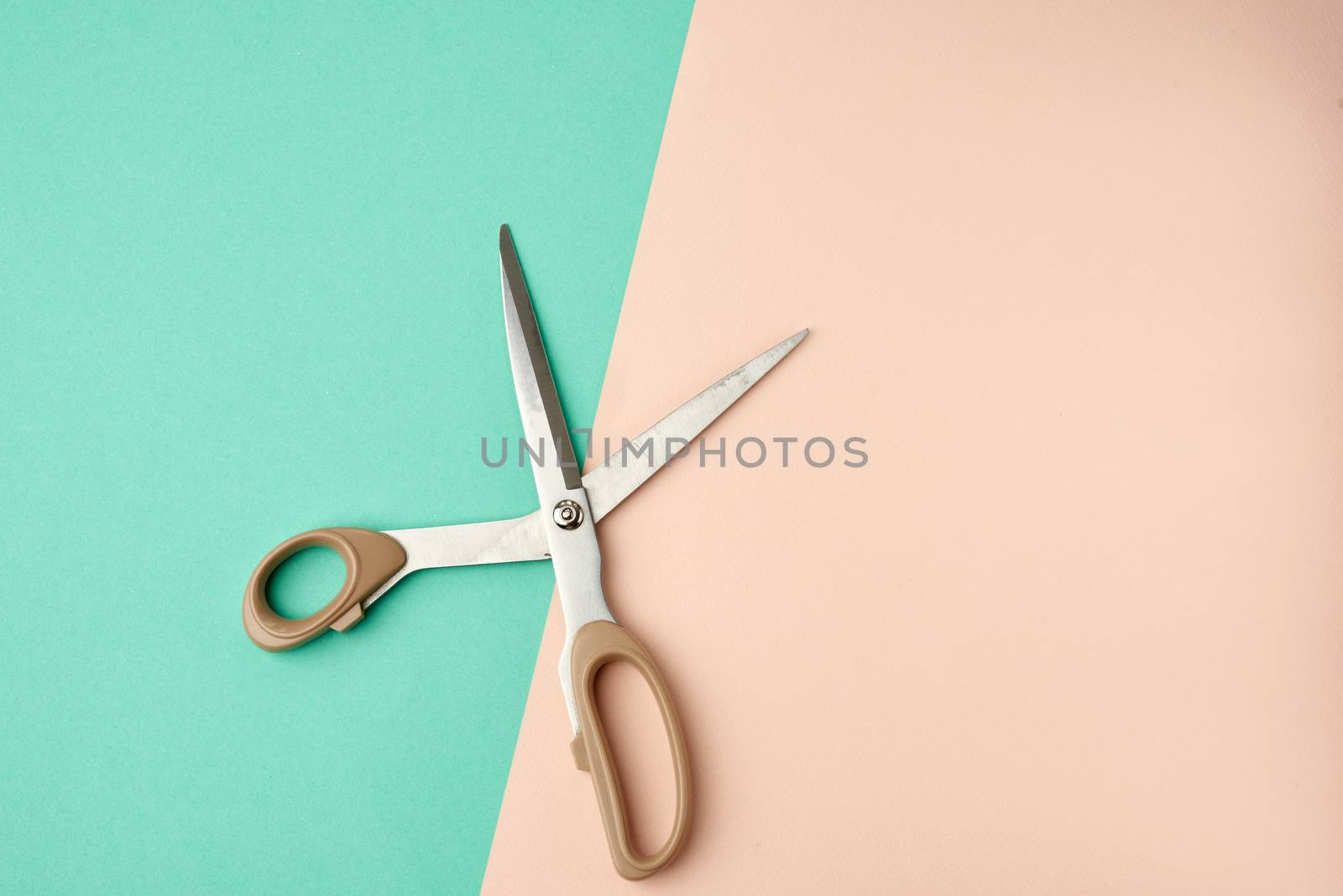 metal scissors with a plastic handle on a green-beige background, top view, flat lay