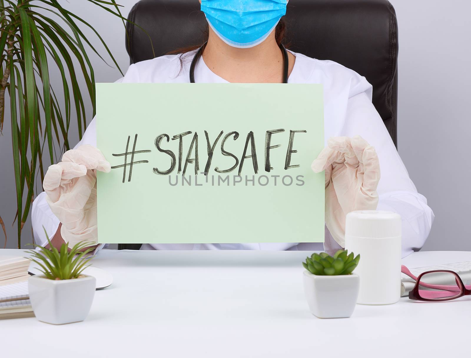 woman doctor in a white coat, sterile medical gloves holds a poster with the inscription stay safe, concept of self-isolation during a pandemic and epidemic