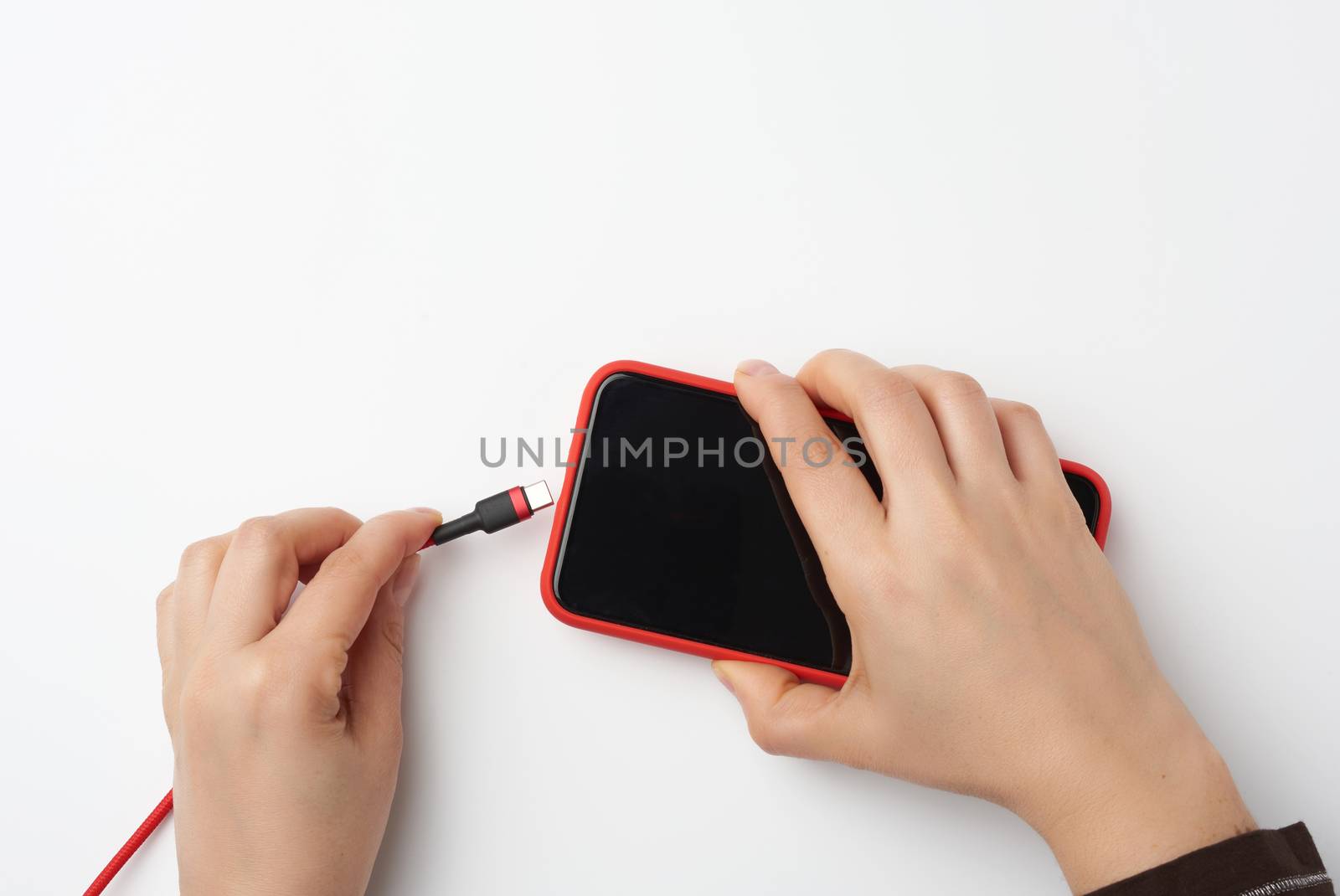 two female hands are holding a smartphone with a blank black screen and cable, charging process, white background, top view