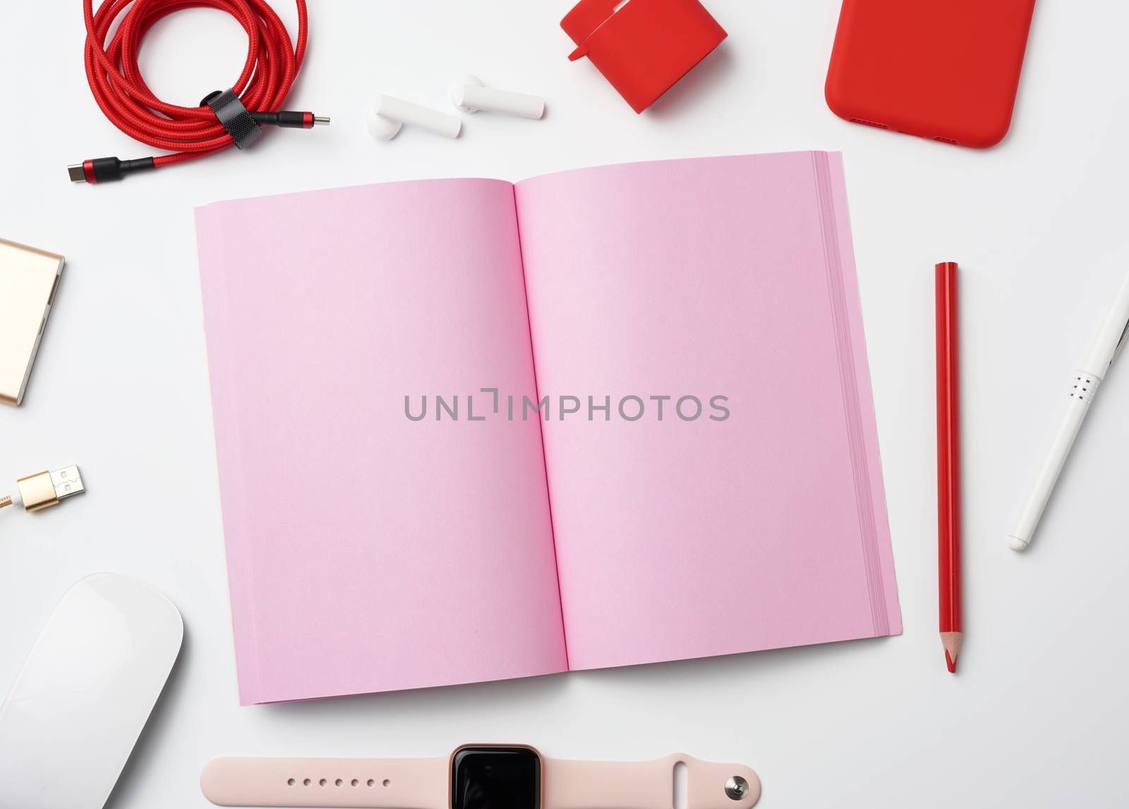 pink paper notebook, power bank with cable, red smartphone, headphones, wireless mouse, smart watch on white background, workplace, top view