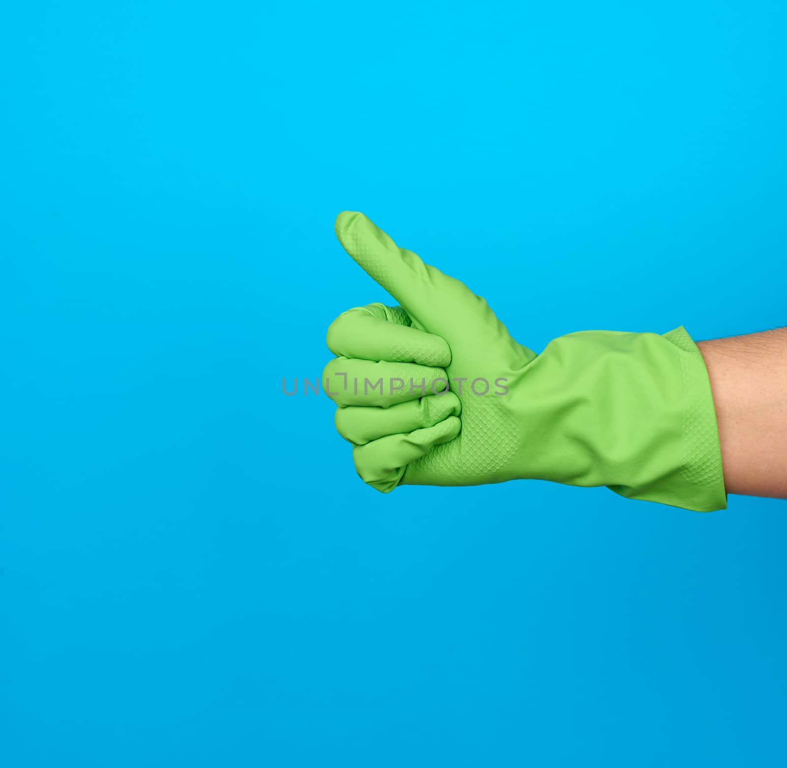 hand in green protective rubber gloves shows gesture like, blue background, positive emotion, consent