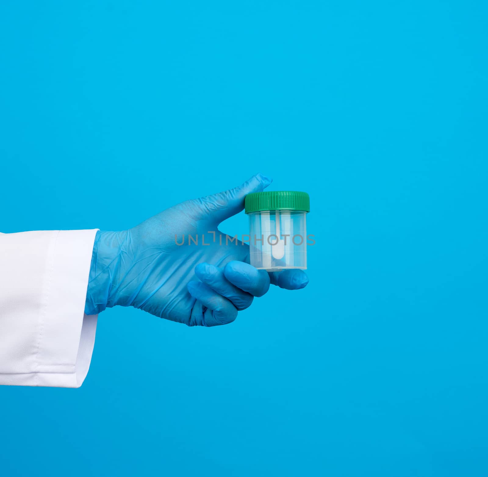 doctor in a white coat and blue sterile latex gloves holds a plastic jar for stool analysis, blue background