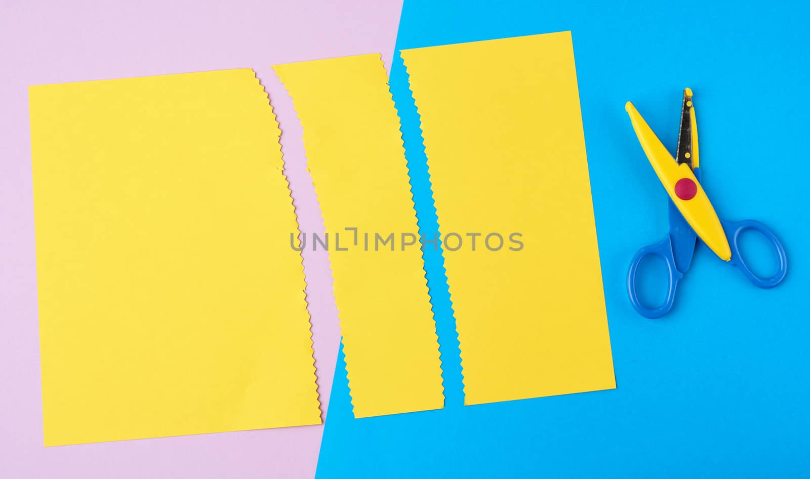 abstract background of colored paper, yellow stripes with a zigzag end and plastic scissors, top view