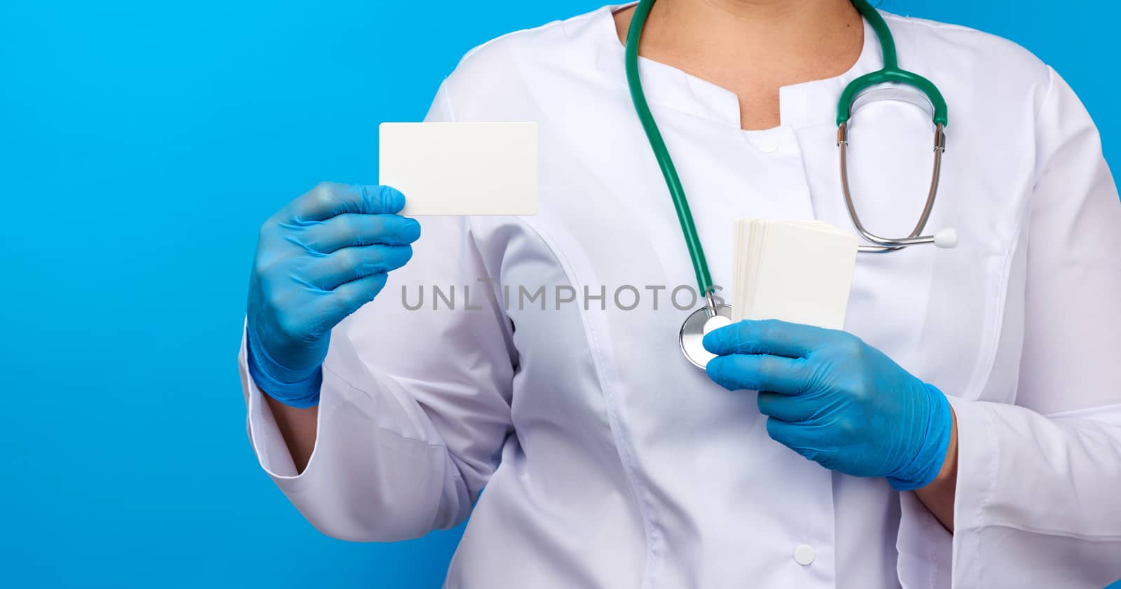 female doctor hand in blue medical latex gloves holds an empty paper business card on a blue background, place for an inscription