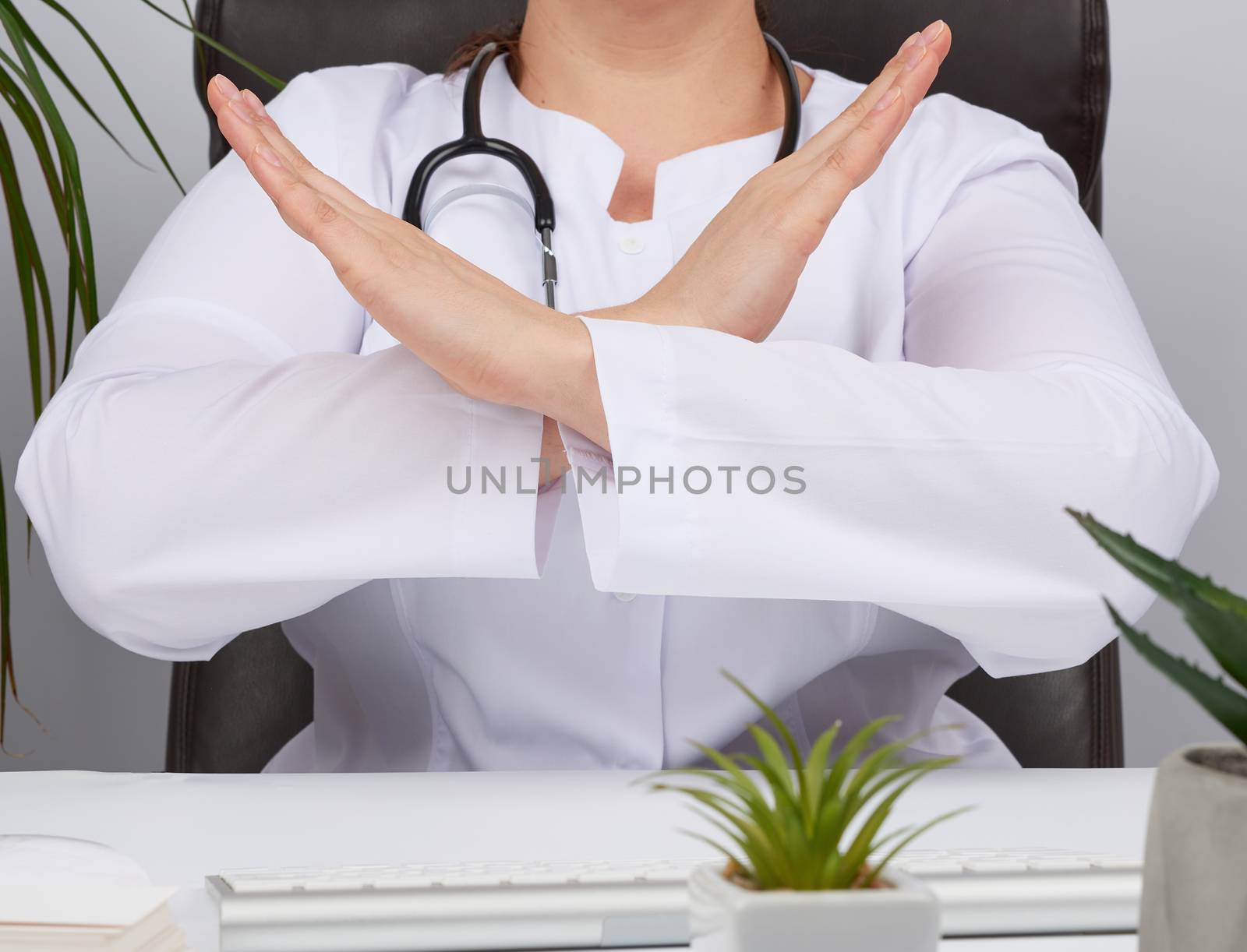 female medic sitting in a brown leather chair in the office and crossed her arms in front of her chest, concept of denial, no