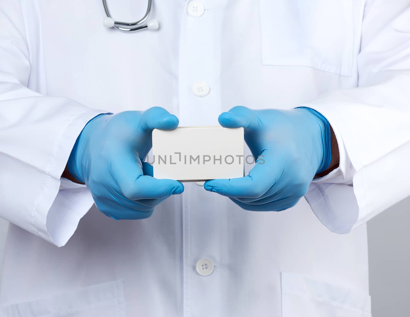 adult doctor therapist is dressed in a white robe uniform and blue sterile gloves is standing and holding a stack of empty white paper business cards, place for inscription