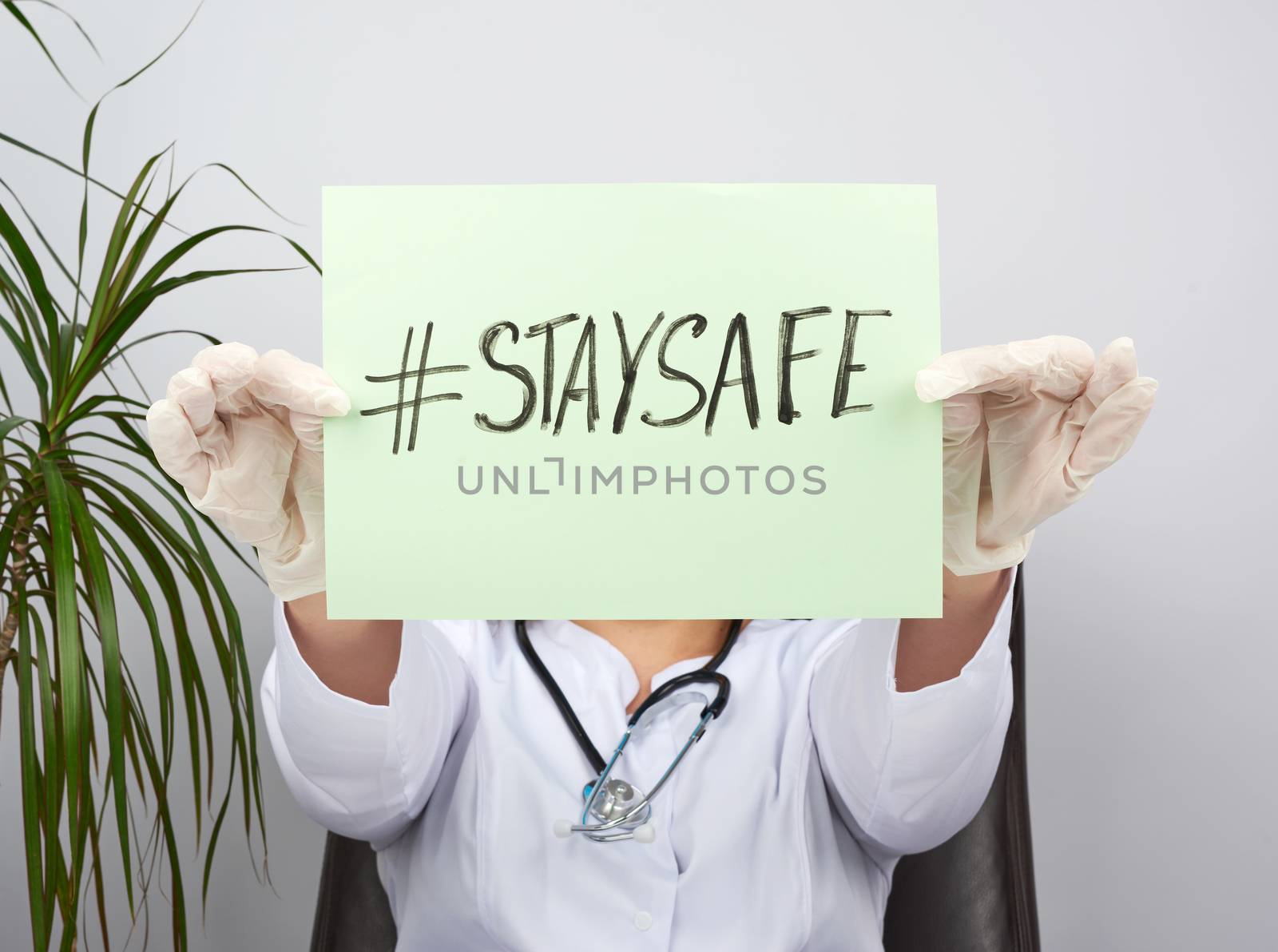 young woman doctor in a white coat, sterile medical gloves holds a poster with the inscription stay safe, concept of self-isolation during a pandemic and epidemic