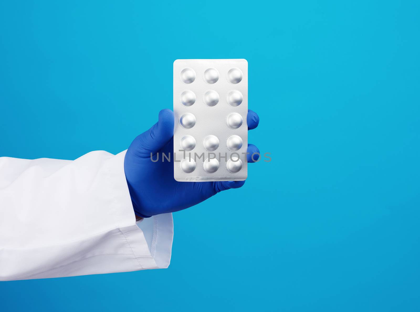 hand with blue sterile gloves holds a pills in a blister, concept for drug treatment of diseases, blue background