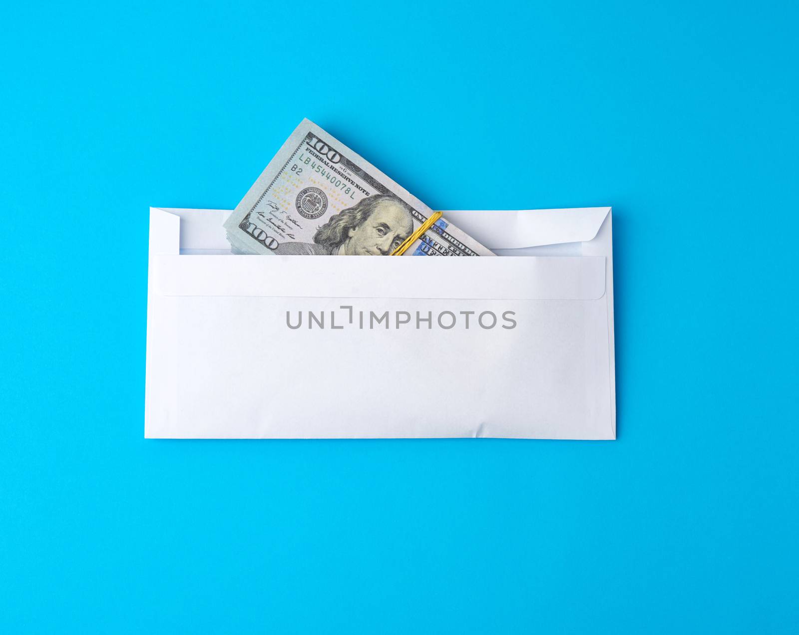 pack of paper American one hundred dollar bills tied with an elastic band and lies in a white envelope on a blue background, concept of a bribe, investment