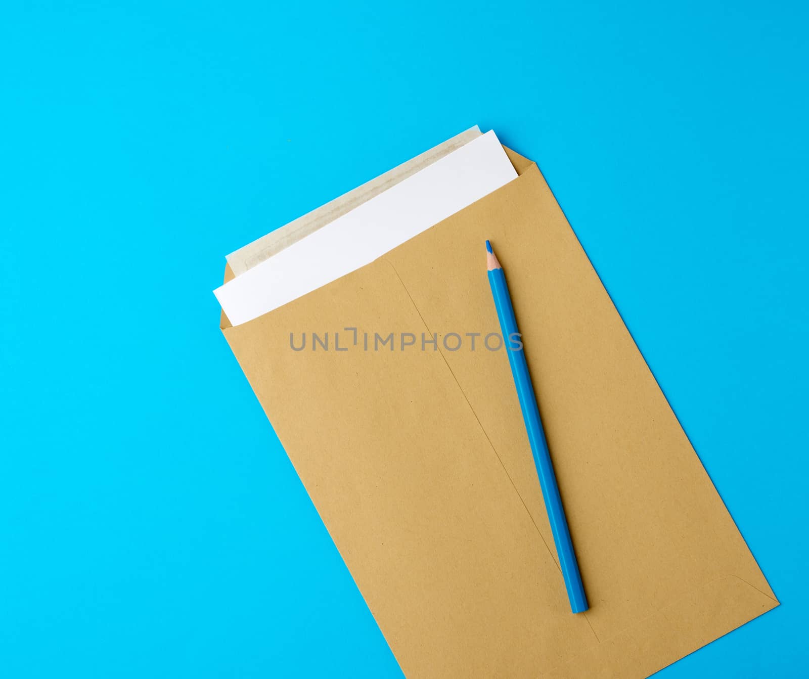 brown blank paper envelope and wooden pencil on a blue background, flat lay