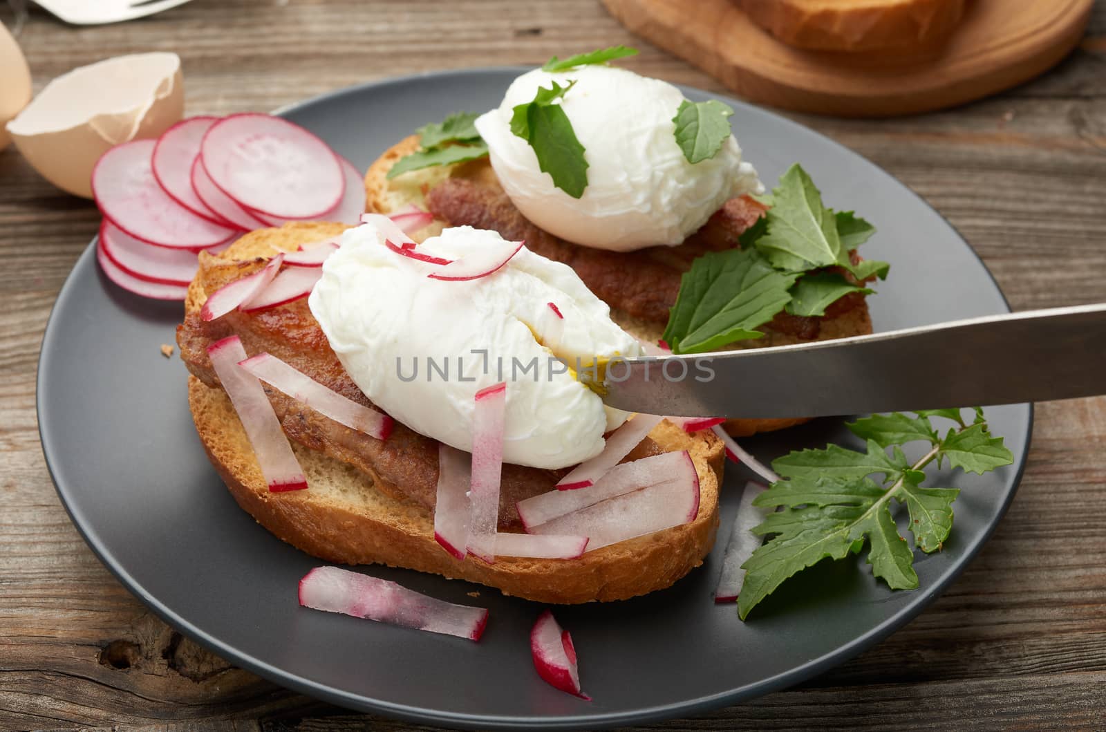 sandwich on toasted white slice of bread with poached eggs, green leaves of arugula and radish, morning breakfast on a gray wooden board, close up