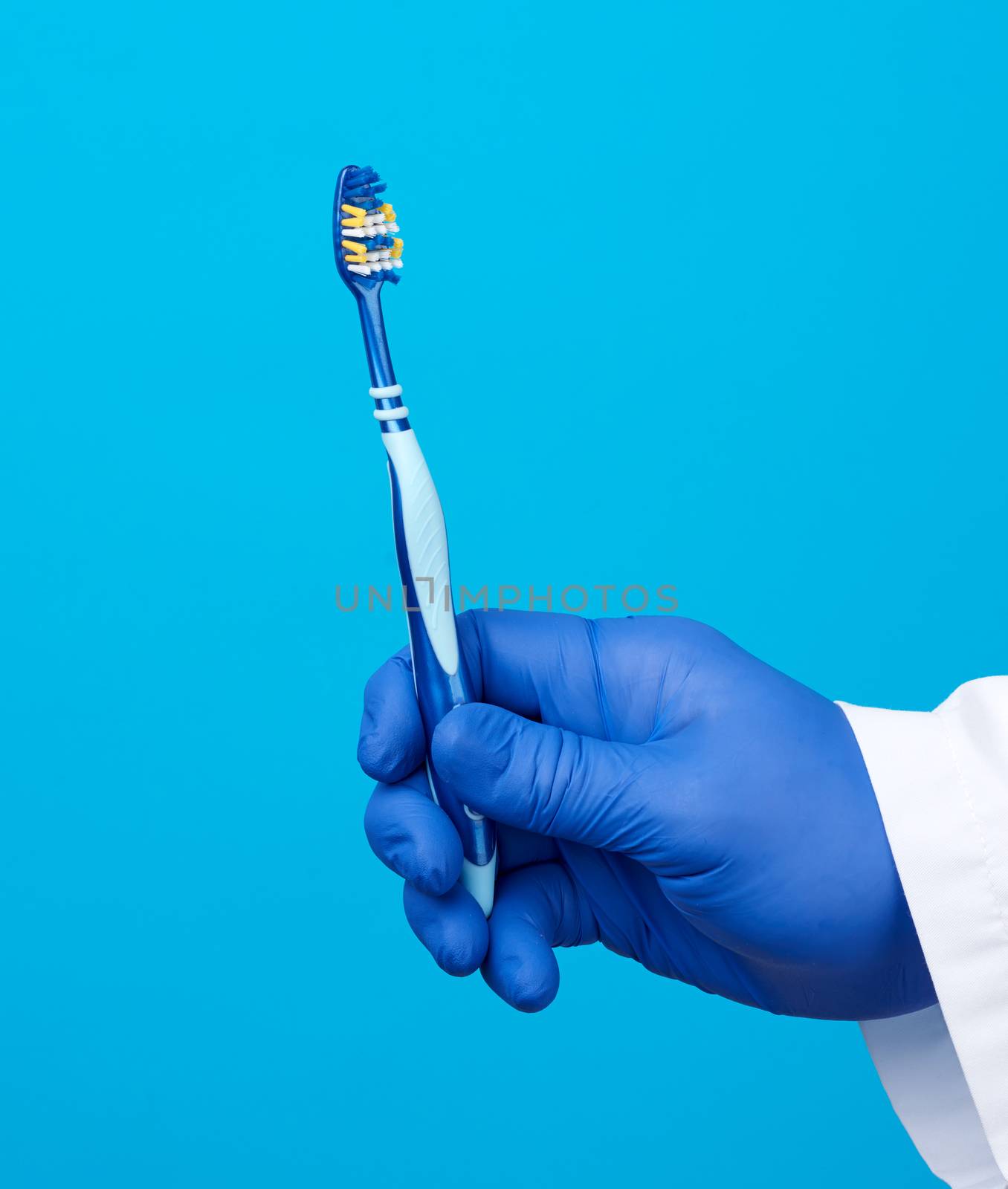 doctor therapist is dressed in a white robe uniform and blue sterile gloves holding a toothbrush, daily brushing concept, blue background