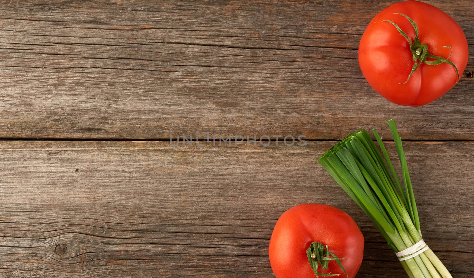 red tomatoes and fresh green onion leaves tied with a rope in a bunch on a gray wooden background, top view