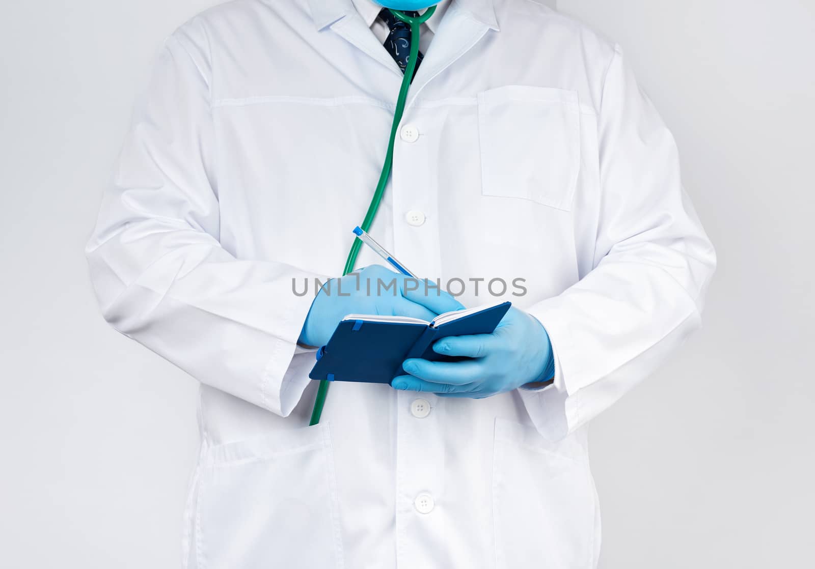 doctor in a white coat and blue gloves holds a blue paper notebook for notes, stethoscope hangs on his neck, white medical backdrop