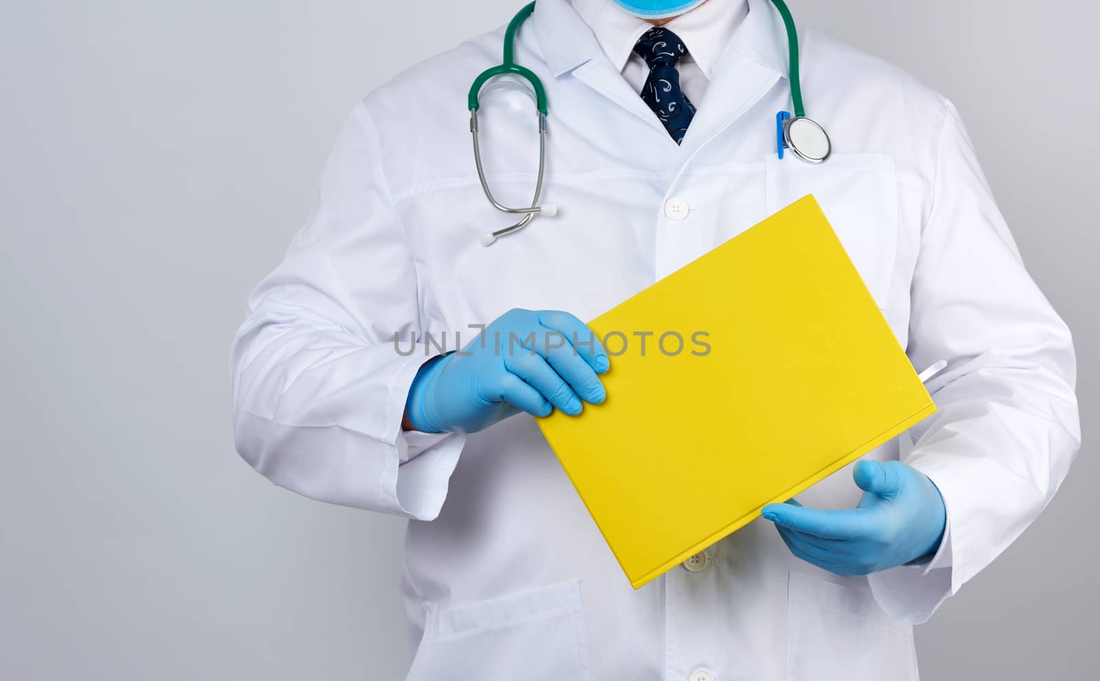 male doctor in a white coat with buttons, wearing blue sterile gloves, holding a yellow paper notebook in his hand on a white studio background