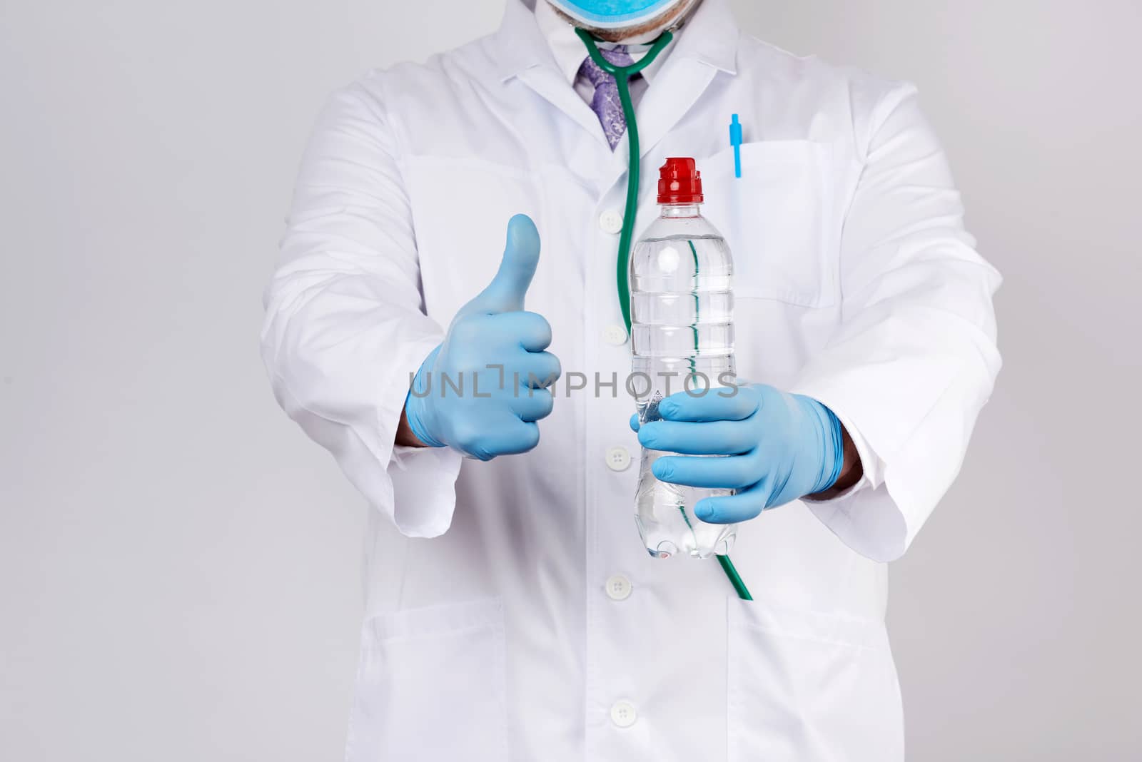 doctor in a white coat and blue latex gloves holds a transparent bottle of water, human consumption concept
