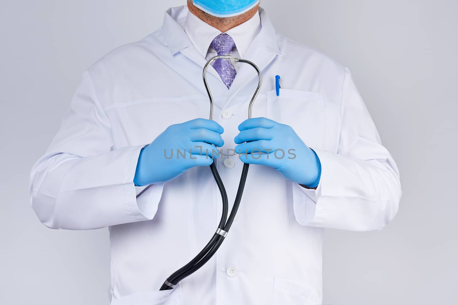 doctor in a white coat and tie holds in his hand a black phonendoscope, wearing blue sterile gloves, white background, medical research