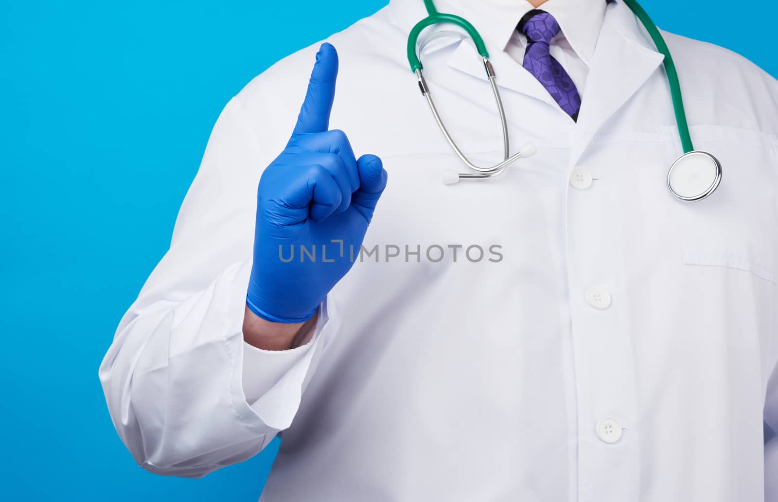 male doctor in white coat, blue medical gloves shows hand gesture of attention, index finger up