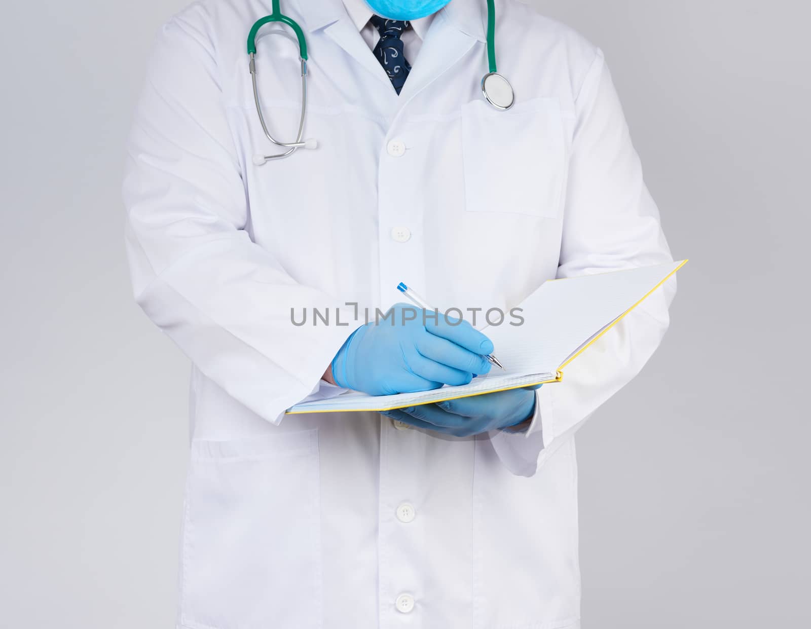 doctor in a white coat, blue latex sterile gloves holds an open yellow notebook in his hand on a white background, concept of recording the diagnosis when visiting patients