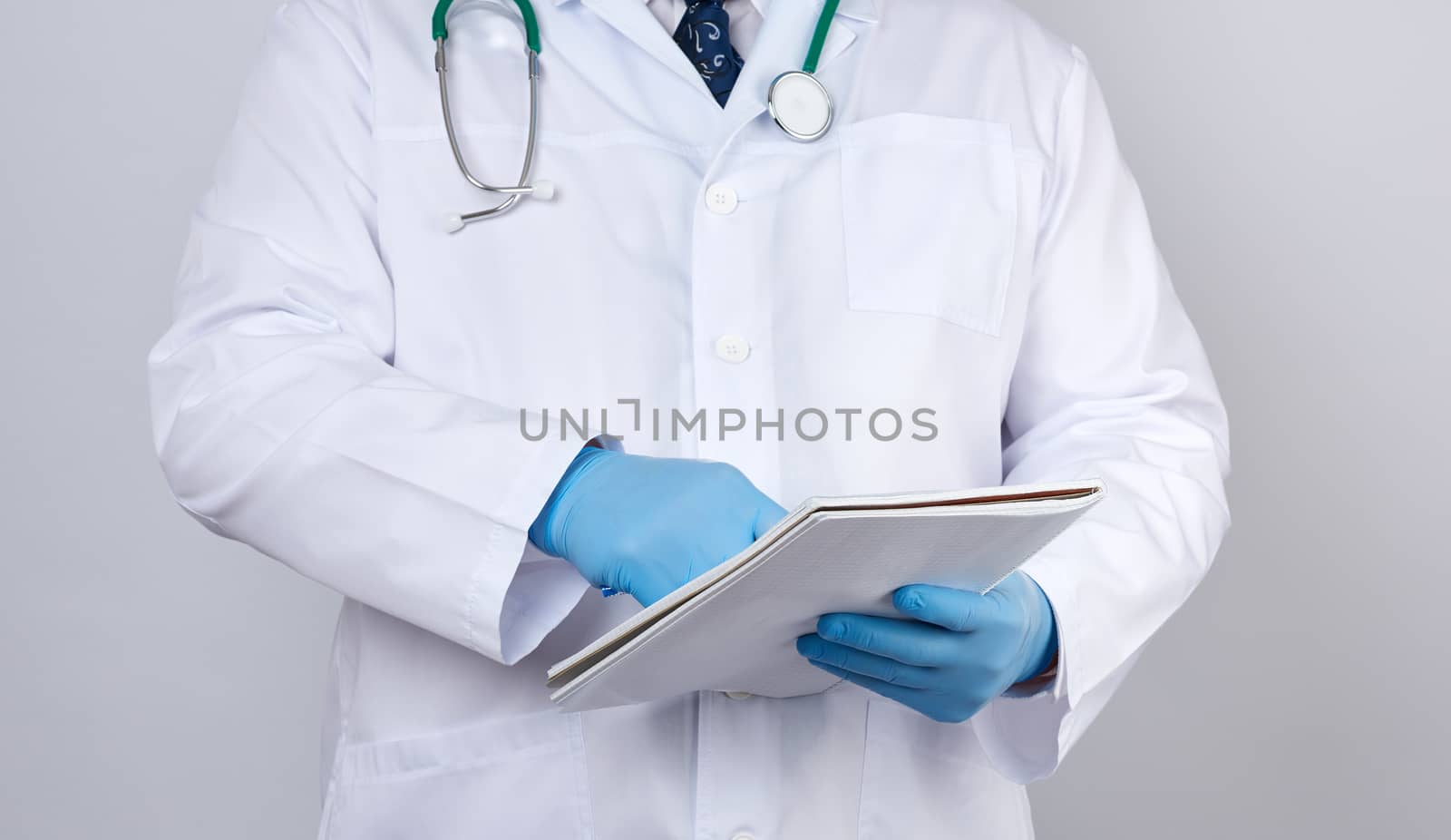 male doctor in a white coat with buttons, wearing blue sterile gloves, holding a paper notebook in his hand on a white studio background