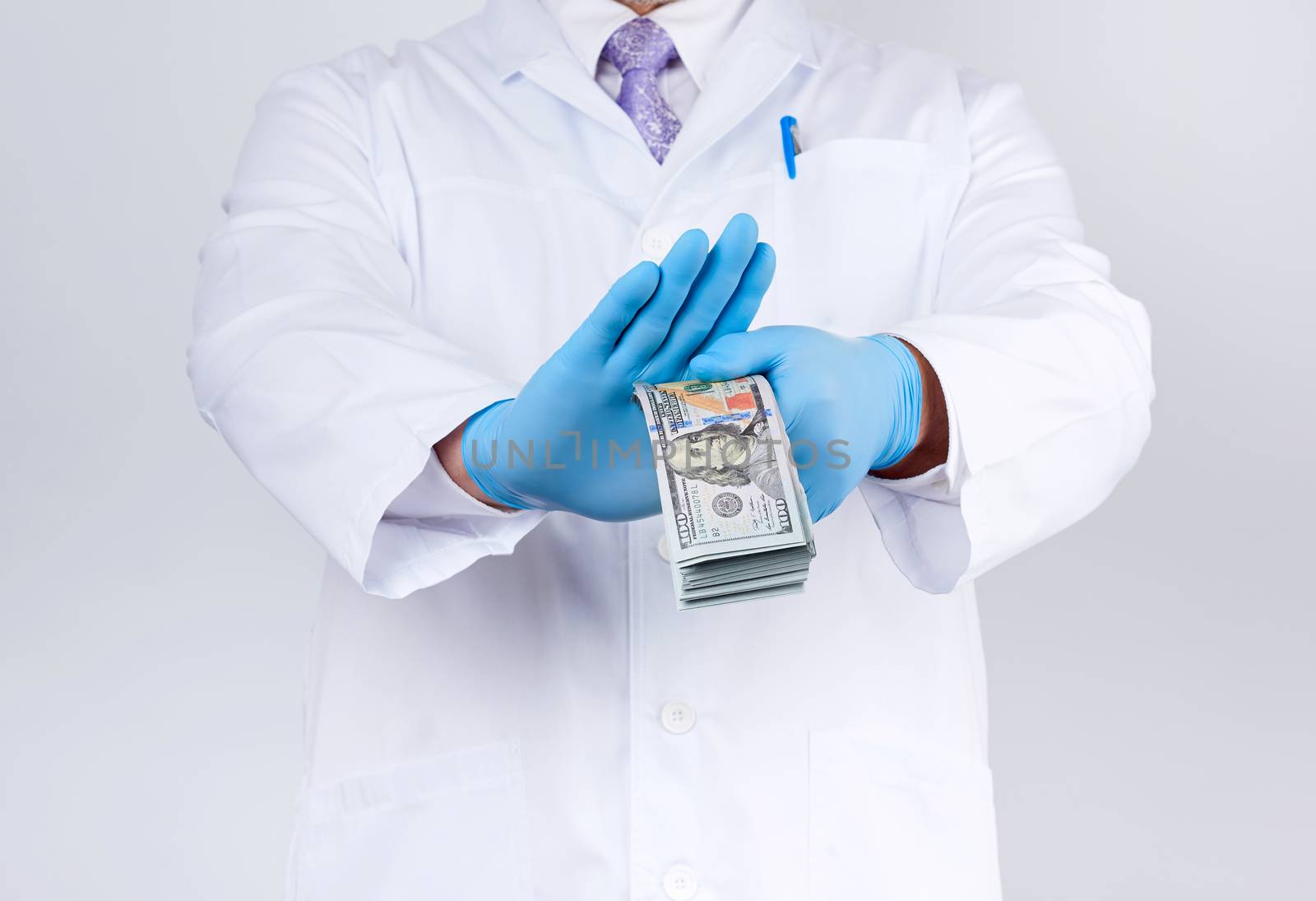 doctor in a white coat and tie, wearing blue sterile gloves, doctor holds a pack of paper money and refuses to take a bribe, anti-corruption concept