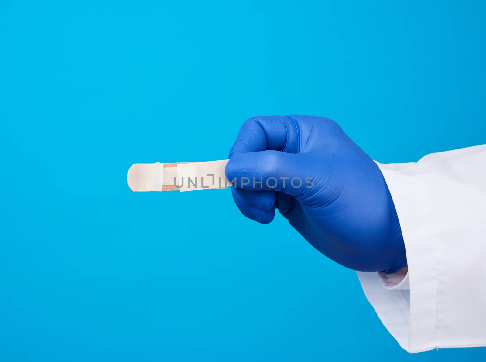 male doctor in a white coat, blue latex medical gloves holds a textile medical adhesive plaster, close up