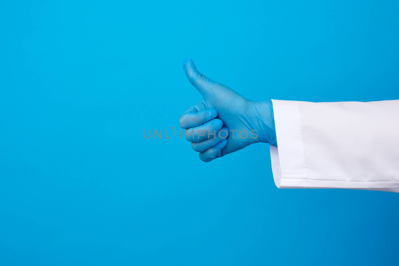 medic woman in white coat, wearing blue medical latex gloves on her hands, showing like gesture in hand, approval concept, copy space