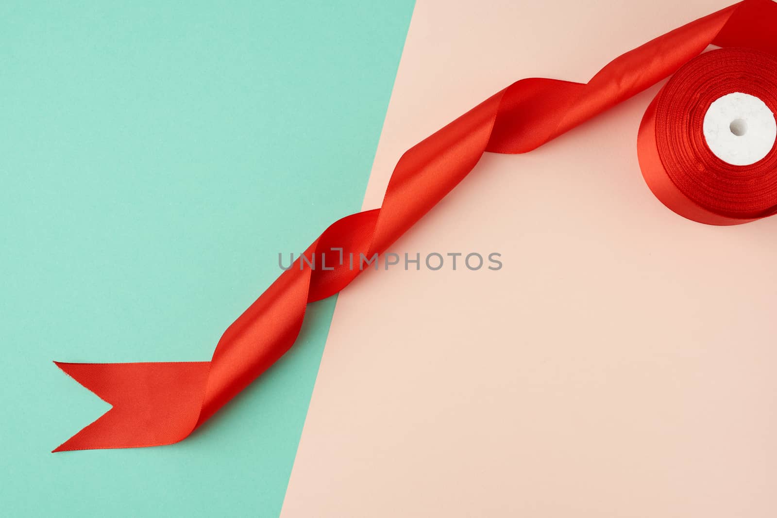 twisted silk red ribbon on a green-beige background, top view, cropped end, close up