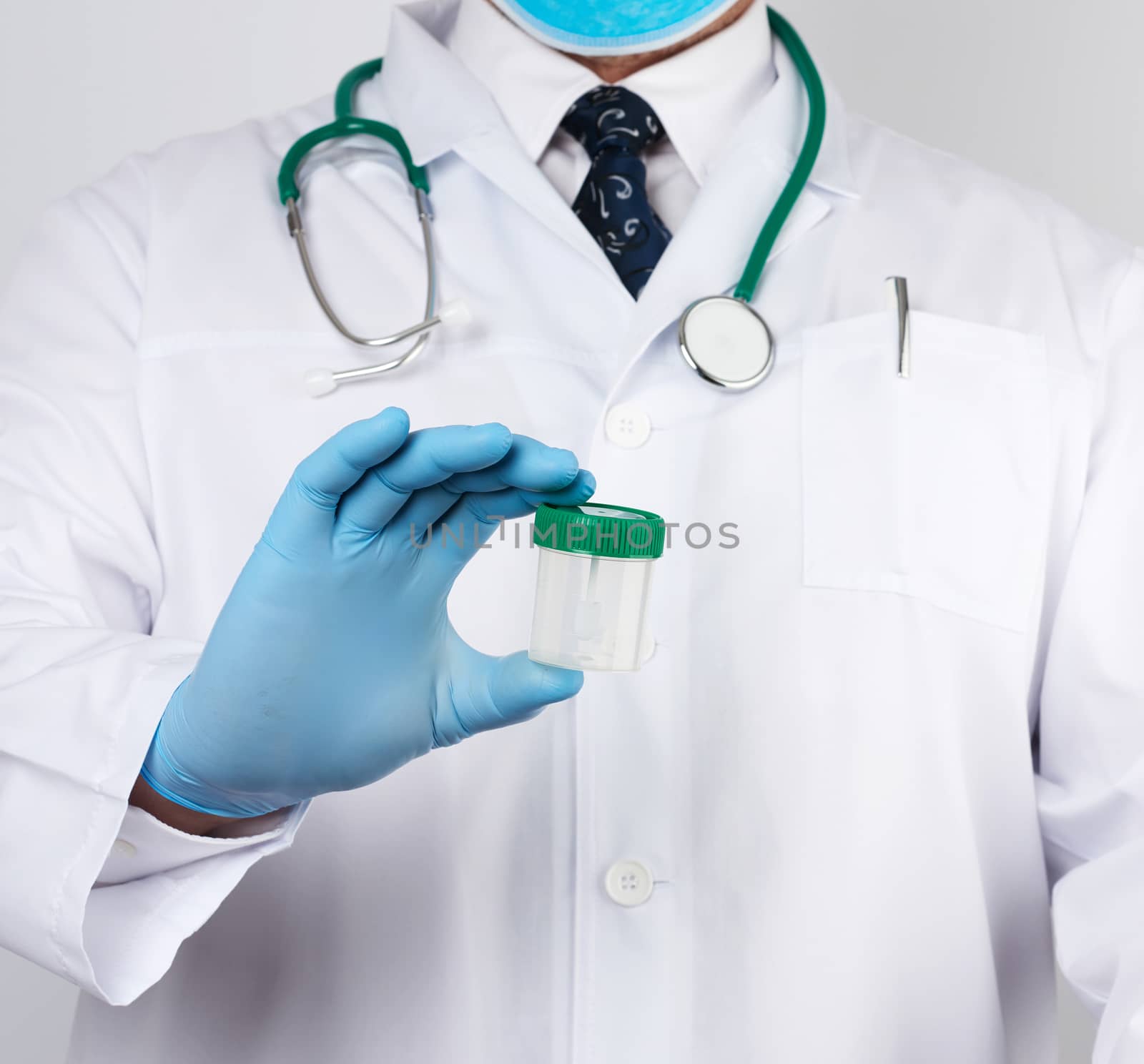 doctor in a white coat and blue sterile latex gloves holds a plastic jar for stool analysis, white background