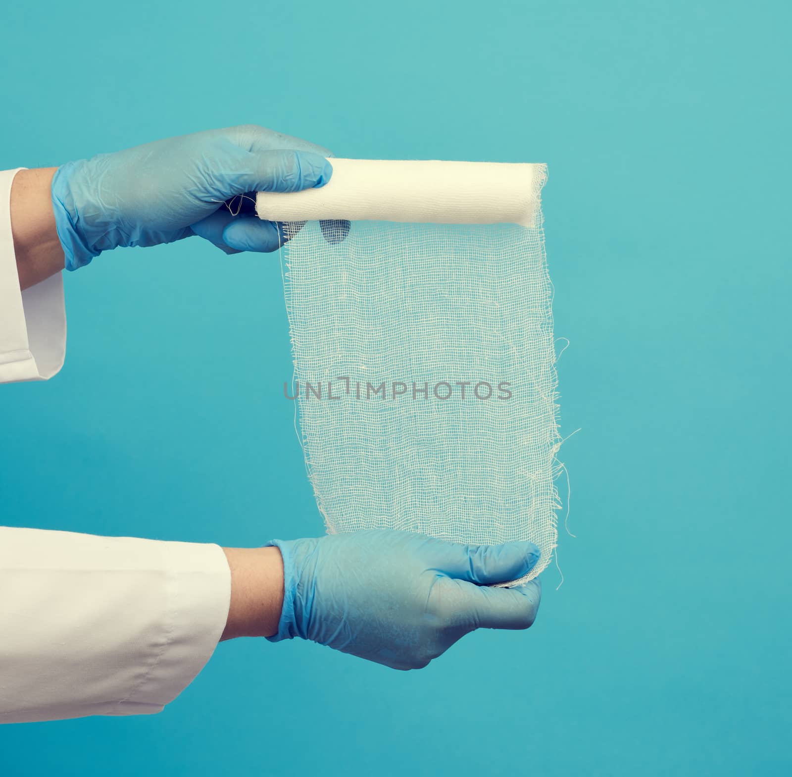 woman in white coat holds a twisted textile gauze bandage, blue background, medical item for bandaging human limbs