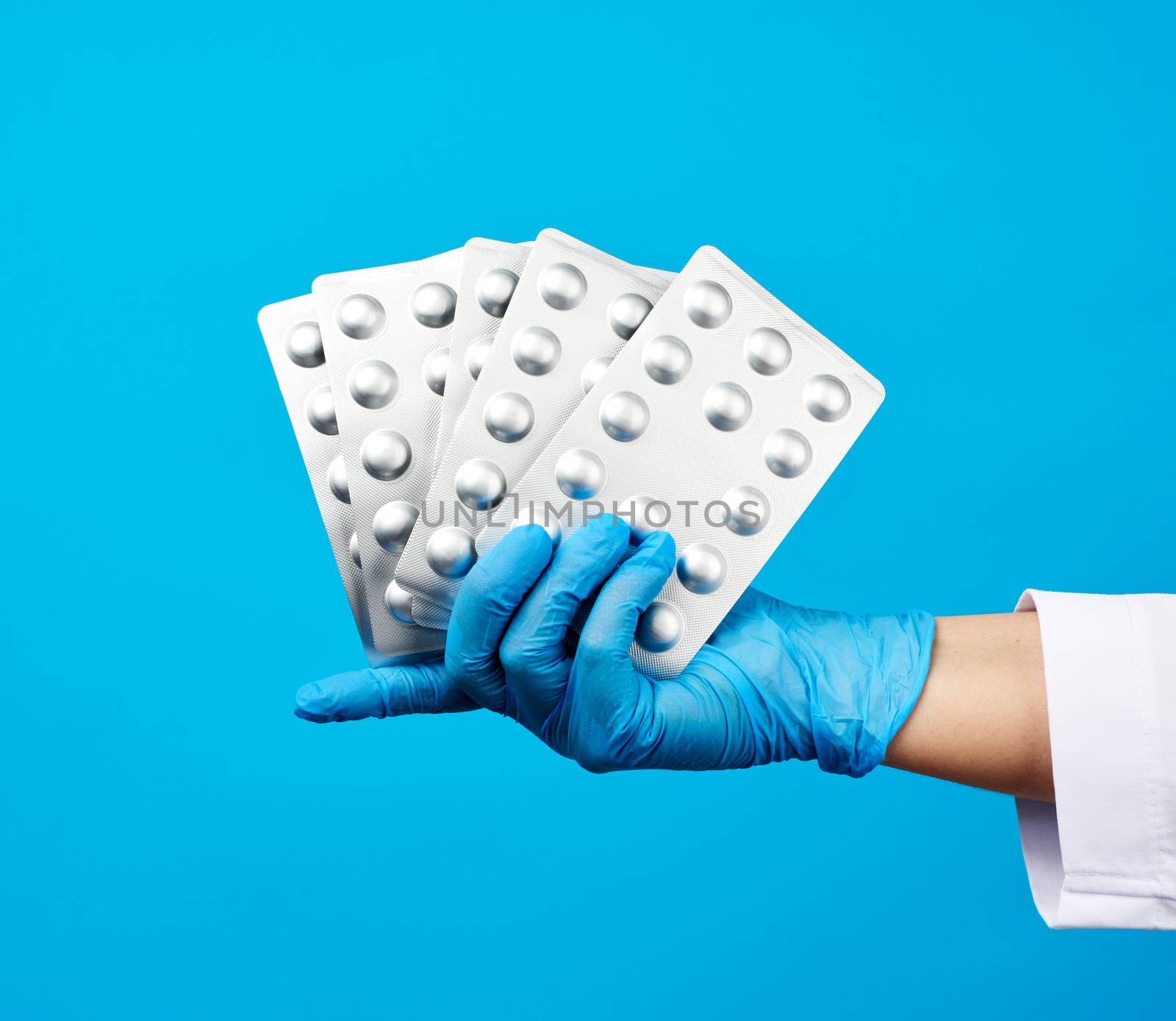 female hand with blue sterile gloves holds a stack pills in a blister, concept for drug treatment of diseases, blue background