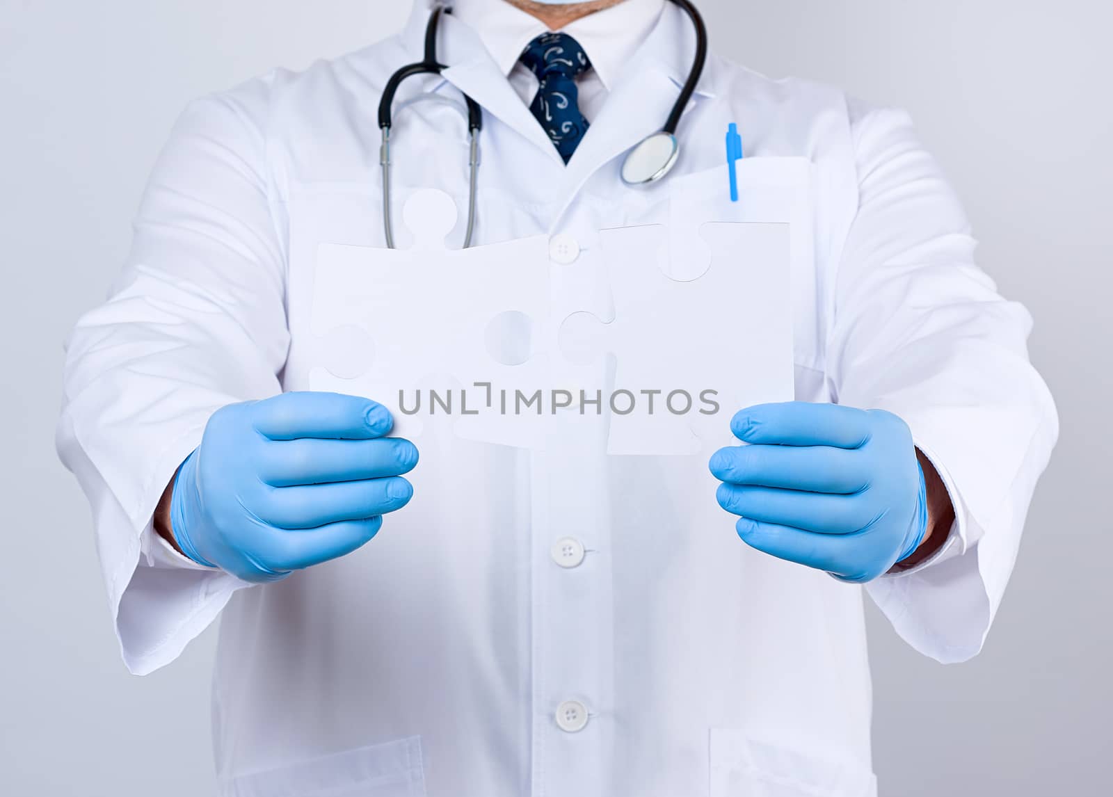 doctor in a white medical coat and blue rubber gloves holds a white paper puzzle, close up