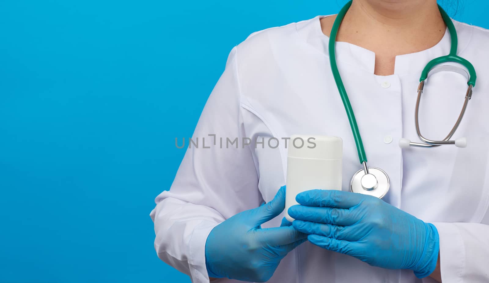 women hand in blue sterile gloves holds a white plastic jar for pills, medical treatment concept for diseases, blue background, copy space
