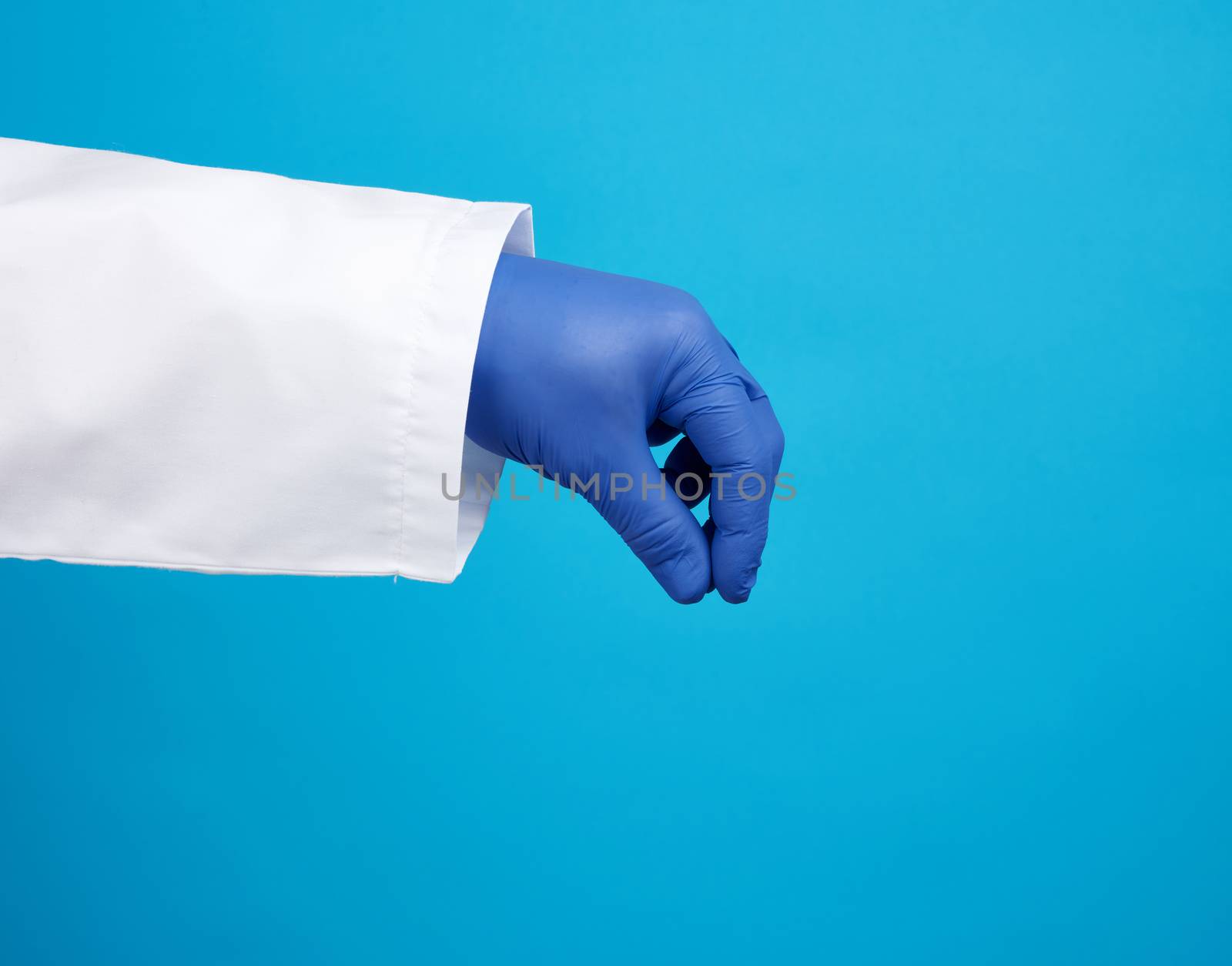 doctor’s hand is wearing a blue sterile rubber glove holding an object, blue background, element for a designer