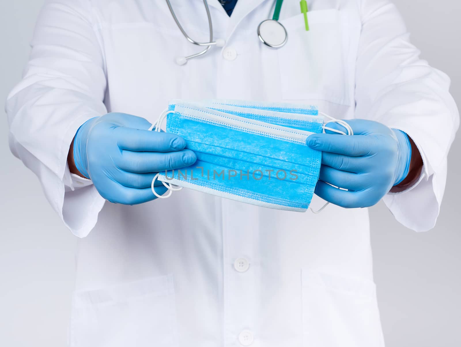 doctor in a white coat, blue latex sterile gloves holds textile medical masks in his hand, protective accessory against viruses and bacteria, close up
