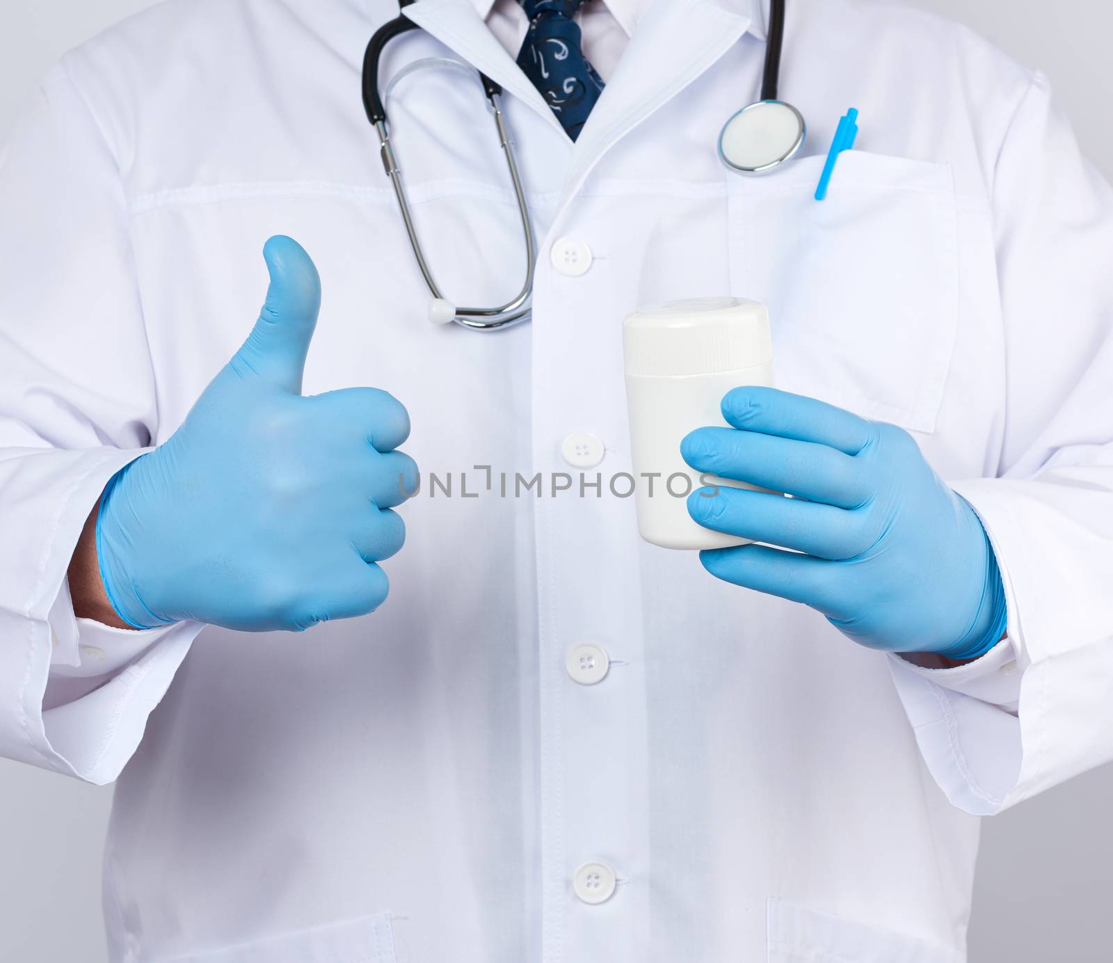 male doctor in a white medical coat and blue latex gloves holds a white plastic jar of pills, close up