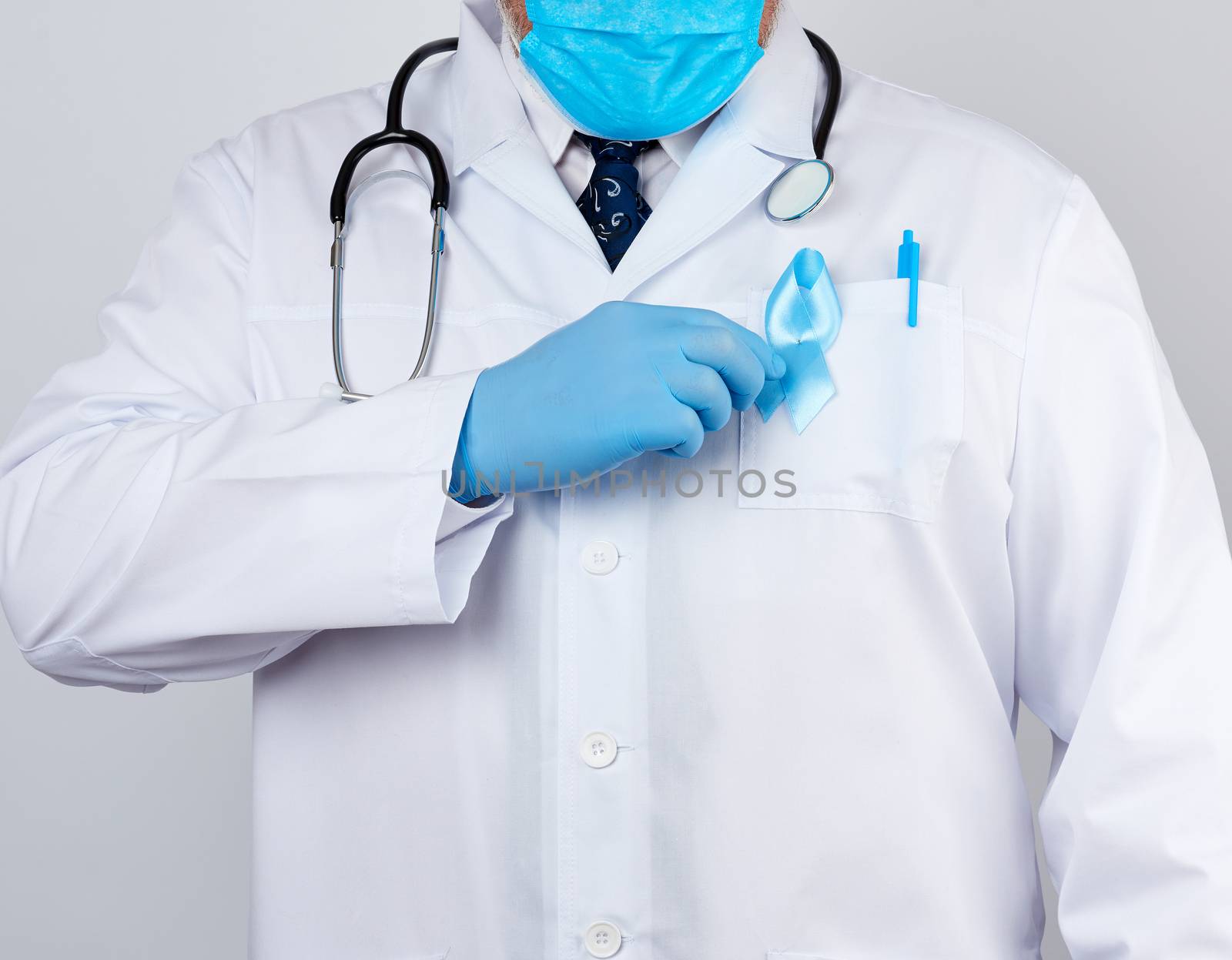 male doctor in a white coat and tie stands and holds a blue silk ribbon in a loop, wearing blue sterile medical gloves, symbol of the fight and treatment of prostate cancer