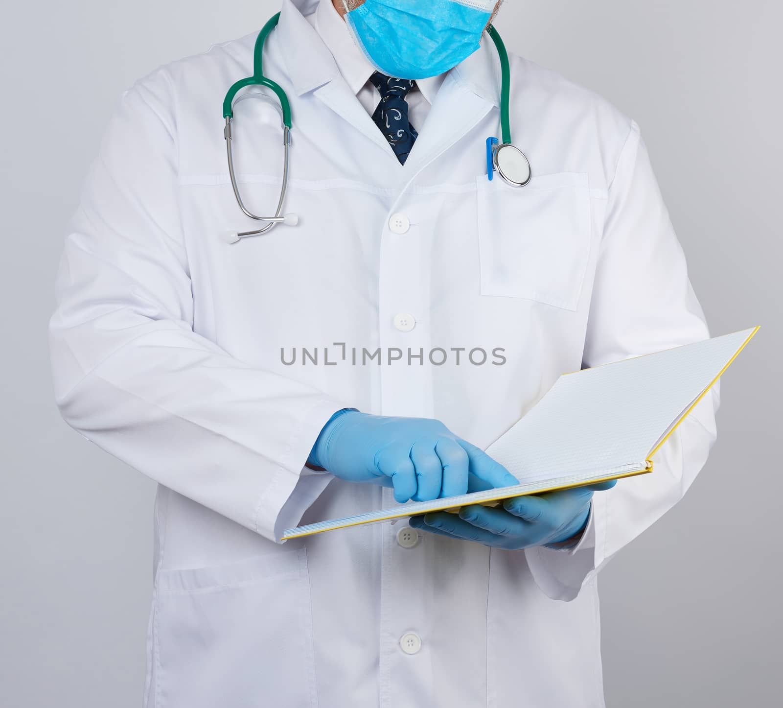 male doctor in a white coat with buttons, wearing blue sterile gloves, holding a paper open notebook in his hand on a white studio background