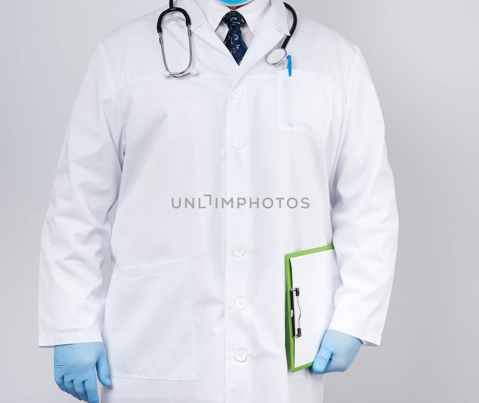male doctor in a white coat, blue latex gloves, a stethoscope hanging on his neck, doctor holding a green paper holder with a white blank sheet