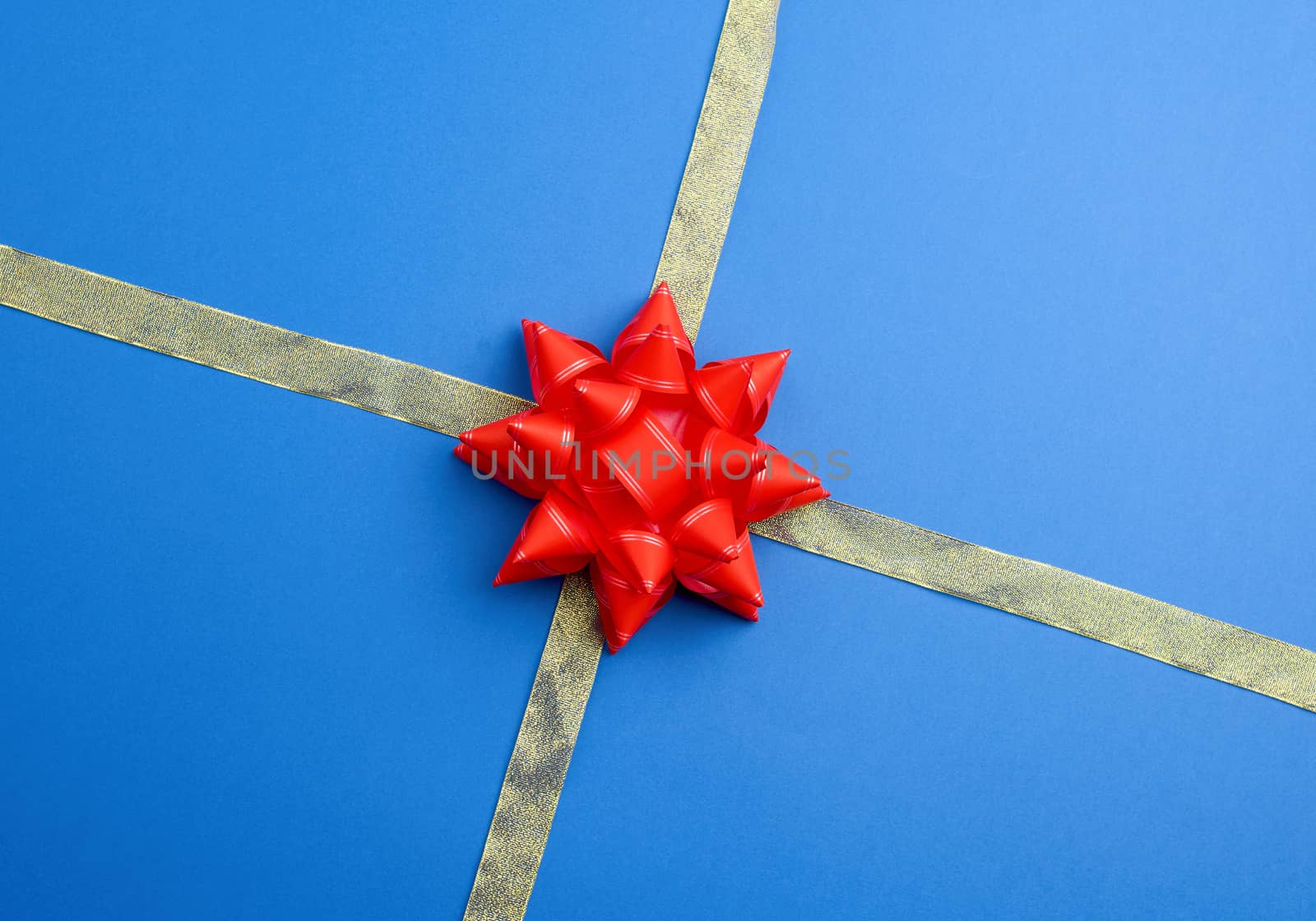 shiny golden silk ribbon crossed on a blue background in the middle of a red bow, imitation of tying a gift, top view