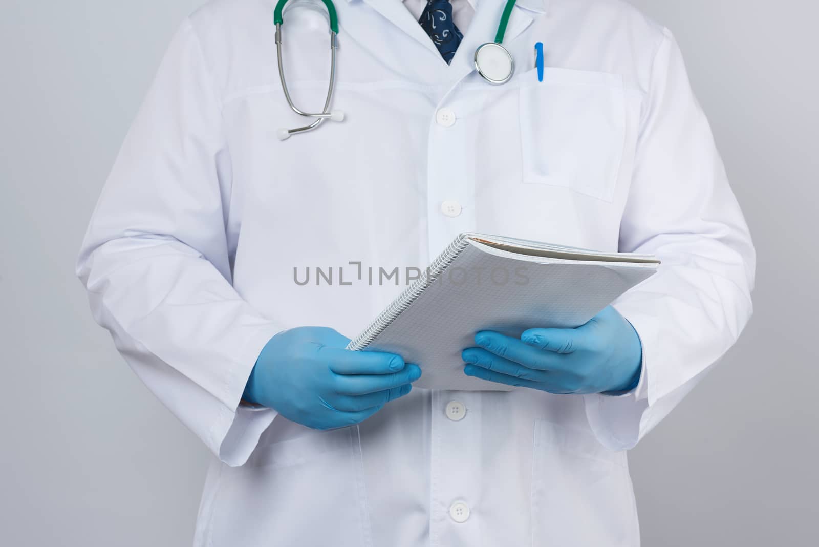 male doctor in a white coat with buttons, wearing blue sterile gloves, holding a paper notebook in his hand on a white studio background