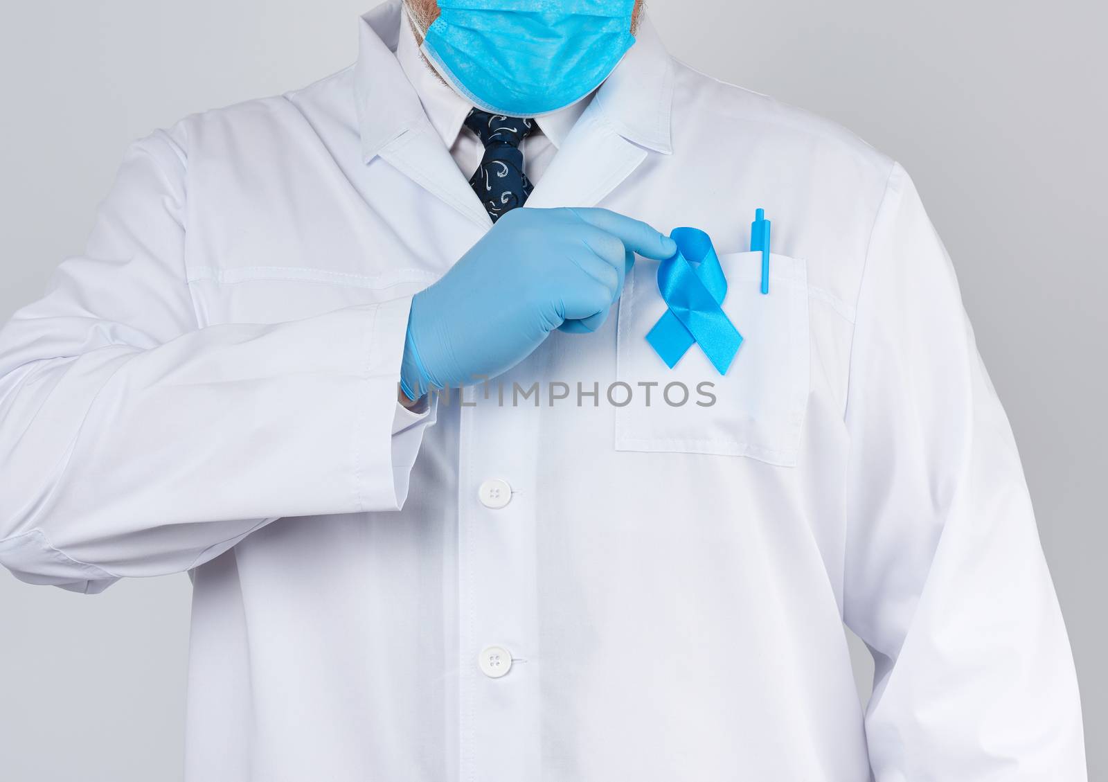 male doctor in a white coat and tie stands. On the pocket pinned a blue ribbon in the shape of a loop, symbol of the fight and treatment of prostate cancer