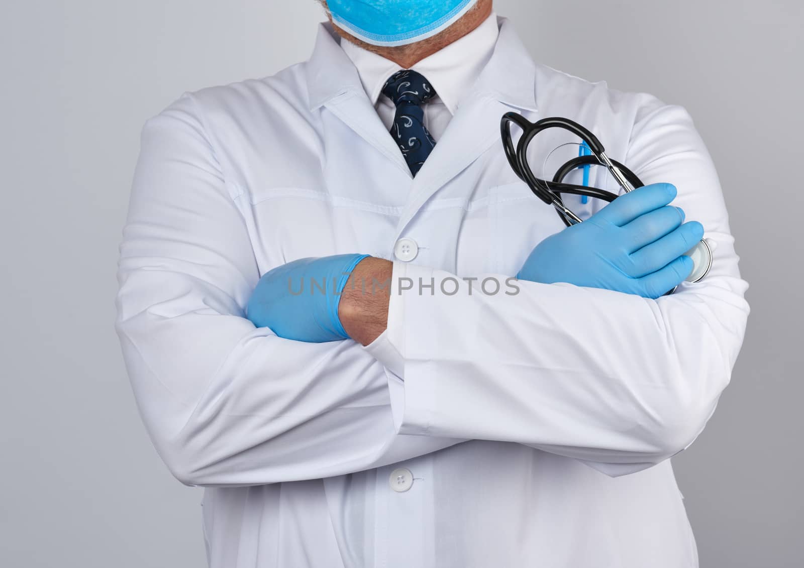adult male doctor in a white medical coat stands and holds a black stethoscope on a white background