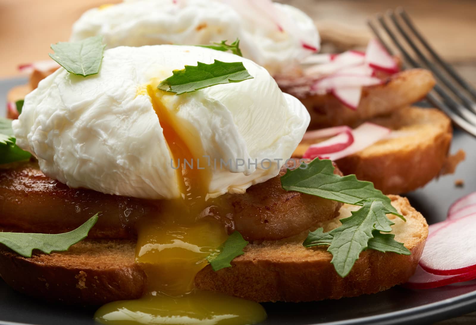 sandwich on toasted white slice of bread with poached eggs, green leaves of arugula and radish, morning breakfast on a brown wooden board, close up