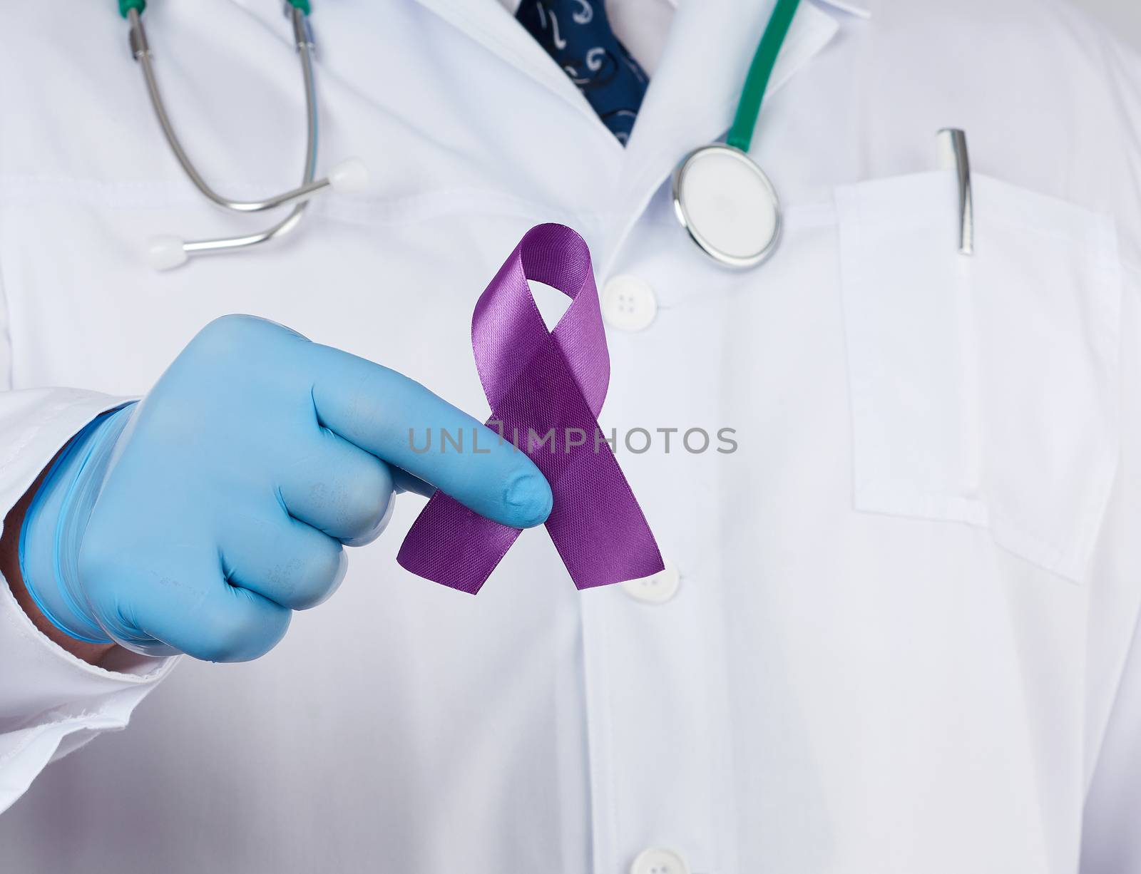 male doctor in a white coat and tie stands and holds a purple silk ribbon in the form of a loop, wearing blue sterile medical gloves. Symbol of early research and disease control, Alzheimer's disease