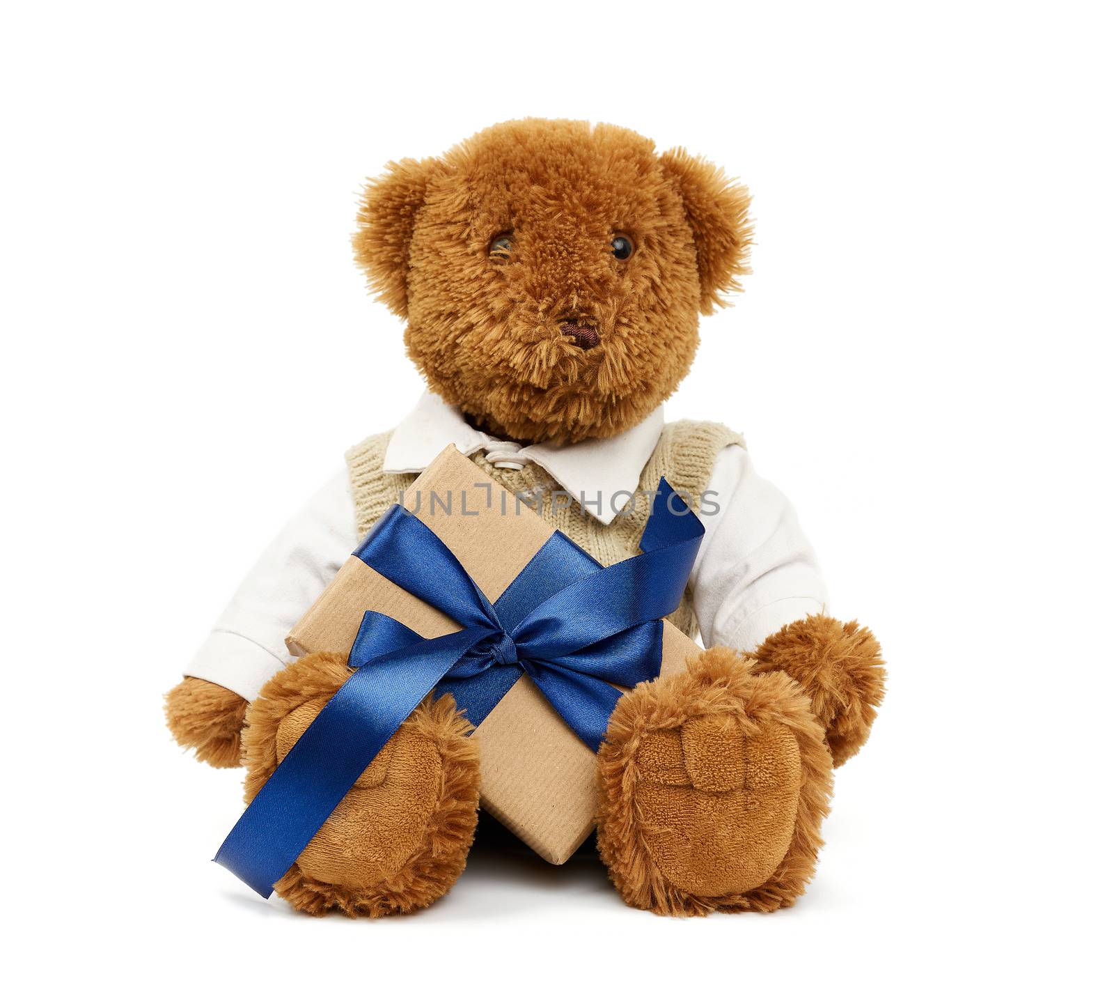 brown teddy bear sits on an isolated white background and holds a box wrapped in brown kraft paper and tied with a blue silk ribbon, festive backdrop