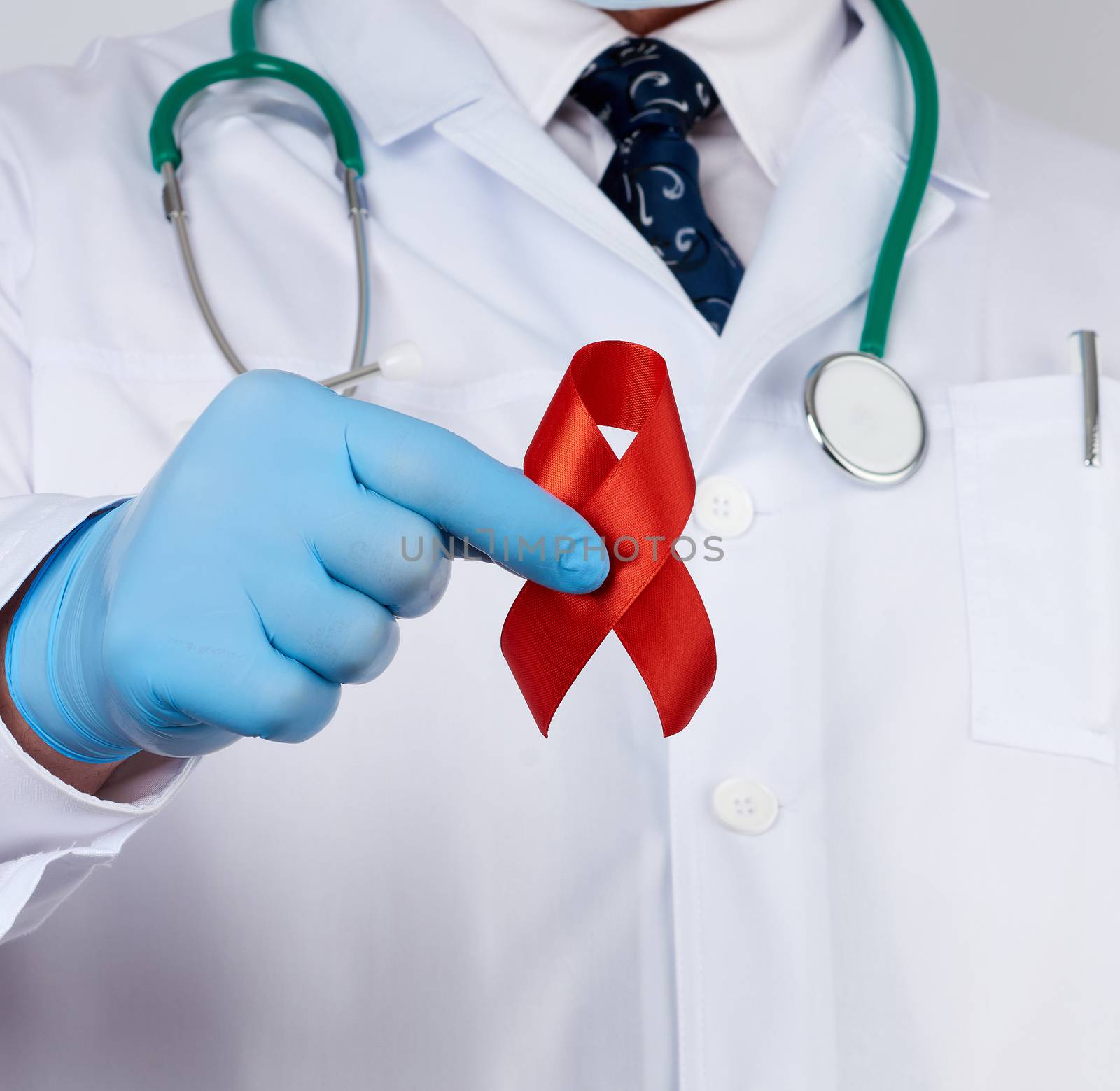 doctor in sterile latex gloves holds a red ribbon-symbol of the fight against disease AIDS and vasculitis, close up